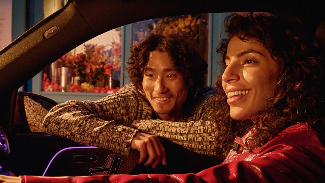 Mladý pár stojí v noci u zaparkovaného vozidla Mercedes-Benz EQB.