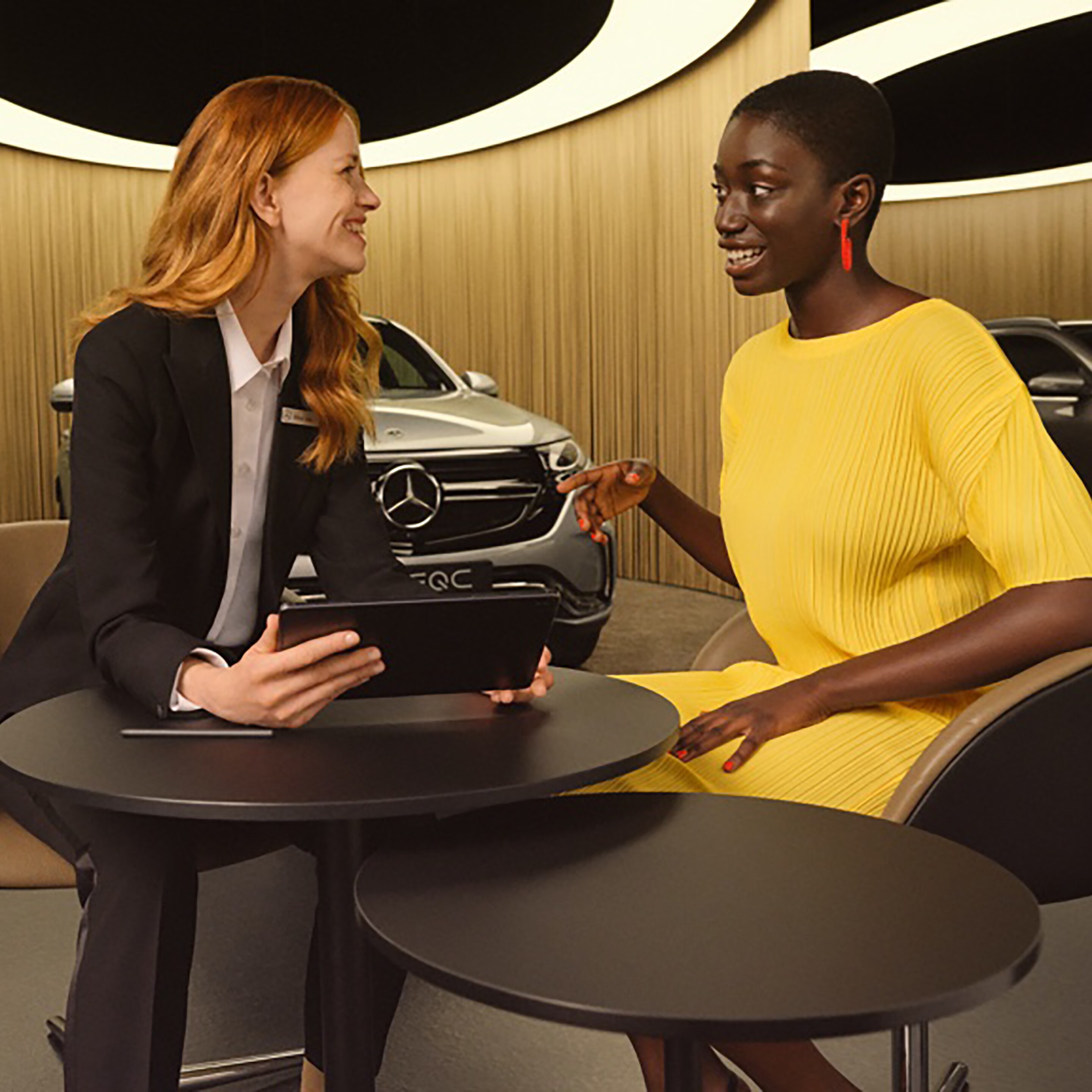 Dvě ženy se na tabletu informují o aplikacích Mercedes-Benz a digitálních doplňcích.