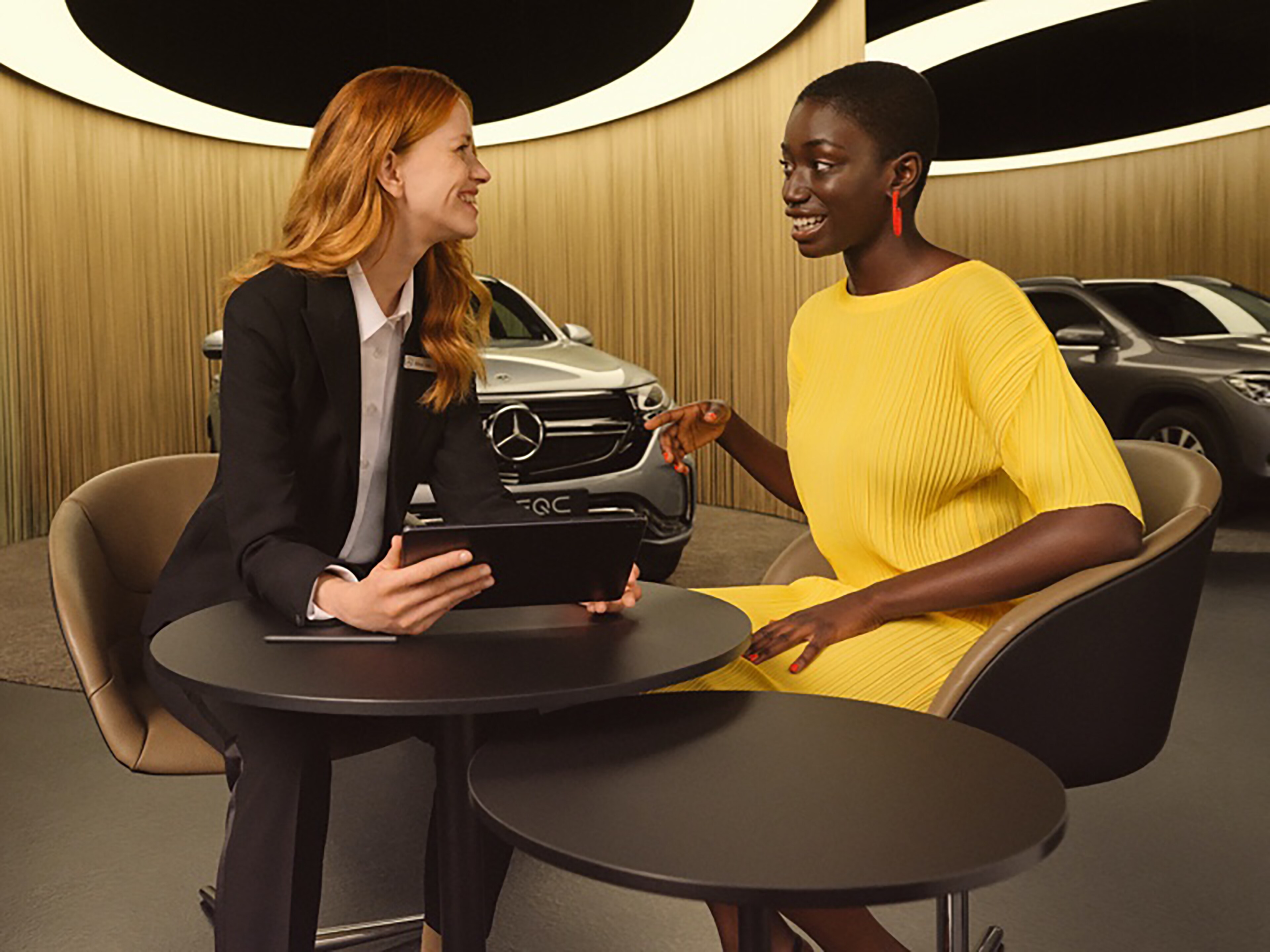 Ženy se na tabletu informují o aplikacích Mercedes-Benz a digitálních doplňcích.