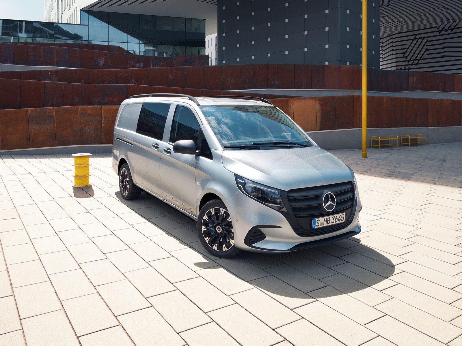 Stříbrné dodávkové vozidlo Mercedes-Benz Vito zaparkované před moderní budovou.