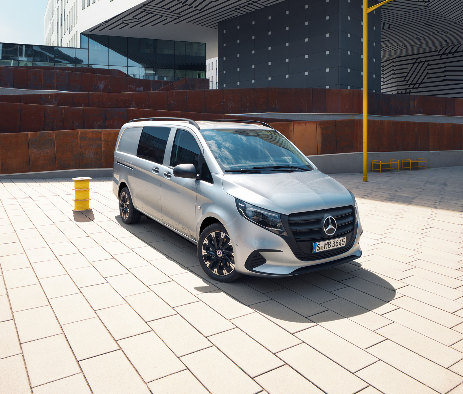 Mercedes-Benz Vito Tourer a Vito Mixto Stříbrné dodávkové vozidlo Mercedes-Benz Vito zaparkované před moderní budovou.