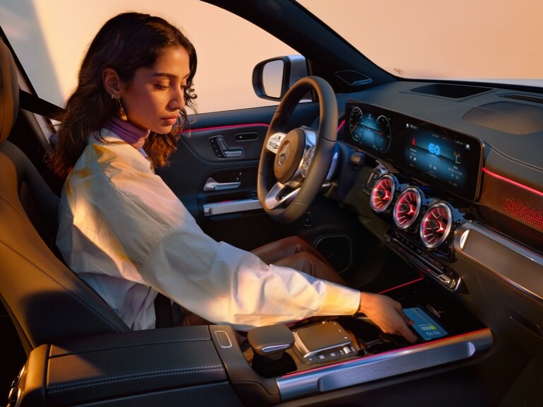 Žena nabíjí svůj chytrý telefon bezdrátově v příručním odkládacím prostoru svého vozu Mercedes-Benz.