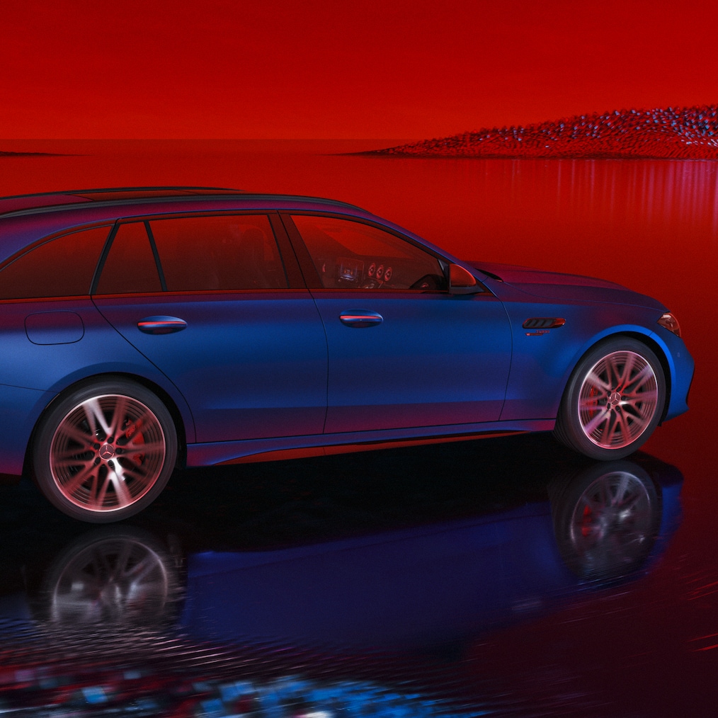 Model Mercedes-AMG C 63 S E PERFORMANCE kombi lakovaný v barevném odstínu MANUFAKTUR modrá spectral magno, při pohledu zepředu před červeným pozadím.
