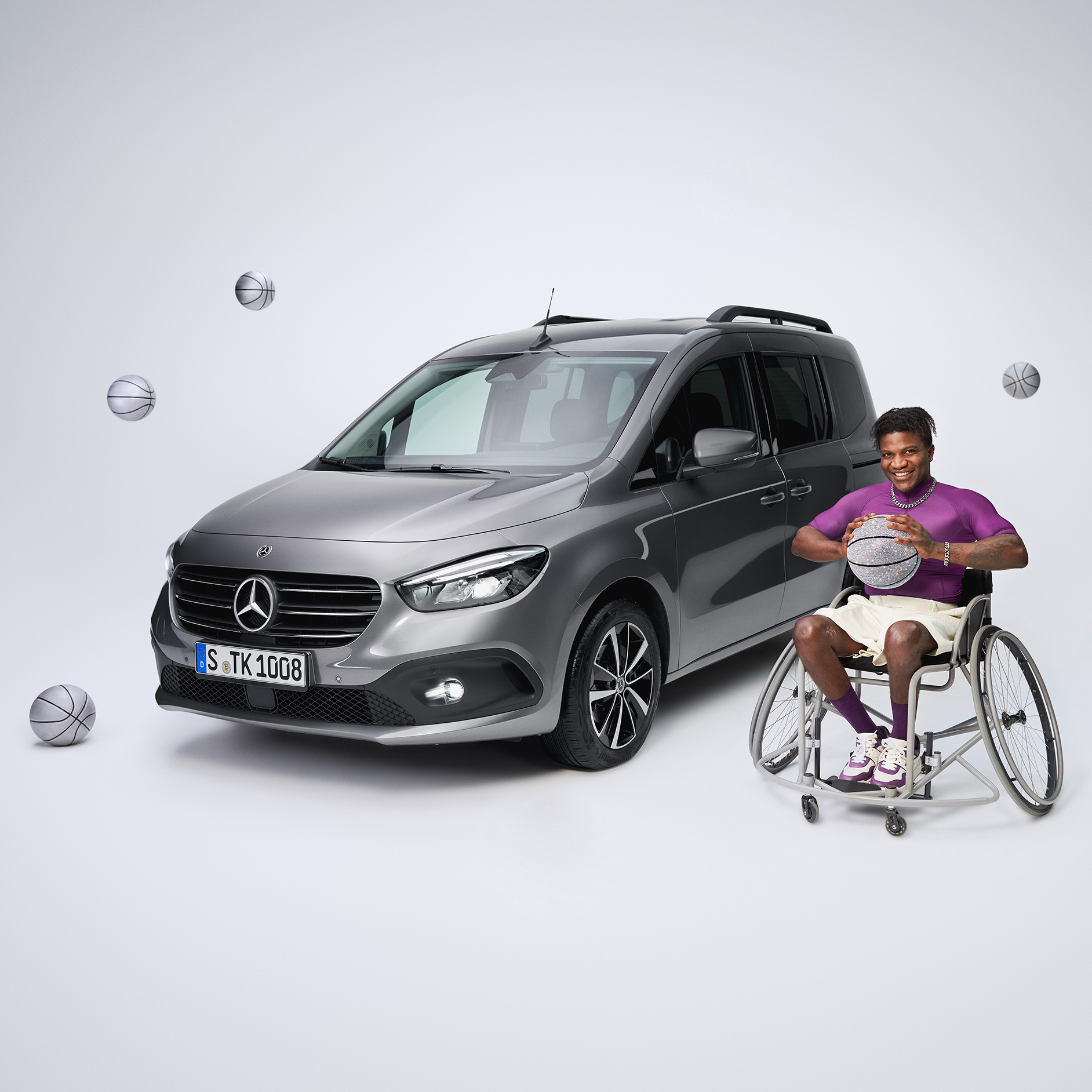Poradenské služby | Jízdní pomocné prostředky | Mercedes-Benz Šikmý čelní pohled na Mercedes-Benz třídy T, který byl upraven pro tělesně postižené, a hráč košíkové na invalidním vozíku v popředí vlevo.