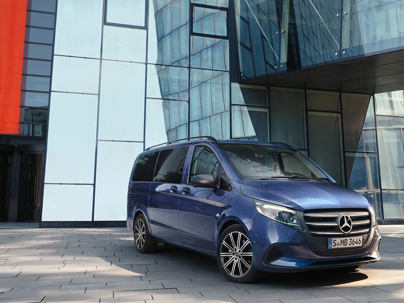 Mercedes-Benz Vito Tourer s posuvnými dveřmi před moderní budovou.