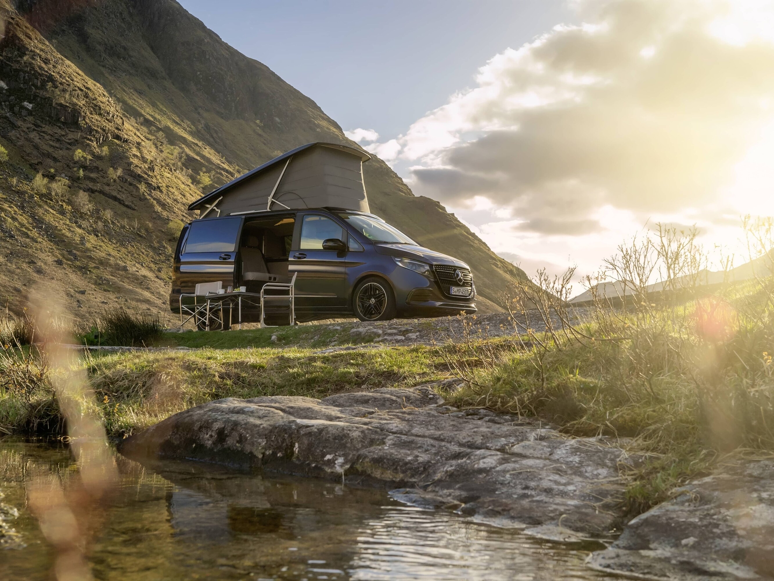 Cestovní automobil Mercedes-Benz Marco Polo s&nbsp;výklopnou střechou zasazený do malebné horské krajiny, demonstrující outdoorové dobrodružství a&nbsp;svobodu života v&nbsp;dodávkovém vozidle.