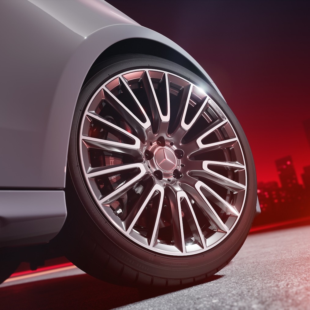 Detailní záběr na kované kolo AMG (RWB) se stříbrně lakovaným třmenem kotoučové brzdy, pohled zespodu před červeným pozadím.