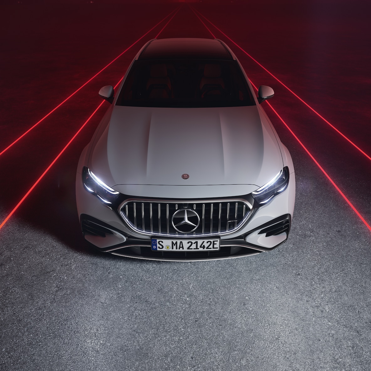Mercedes-AMG E 53 HYBRID 4MATIC+ při pohledu zepředu shora před červeným pozadím.