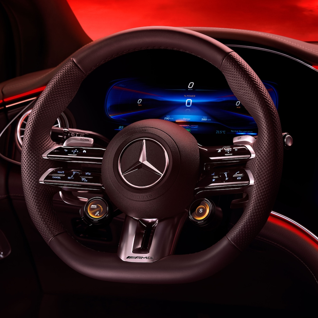 Pohled na volant AMG Performance z perspektivy sedadla řidiče před červeným pozadím.