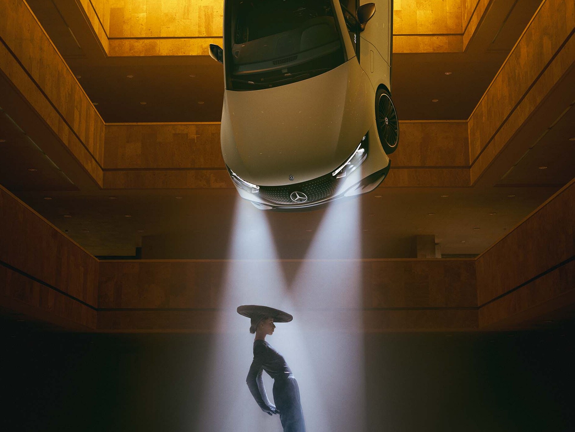 Tmavá místnost, na jejímž stropě visí světlomet, v&nbsp;jehož světelném kuželu stojí žena.