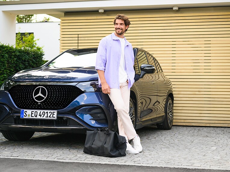 Muž opřený o Mercedes Benz před jeho domem.