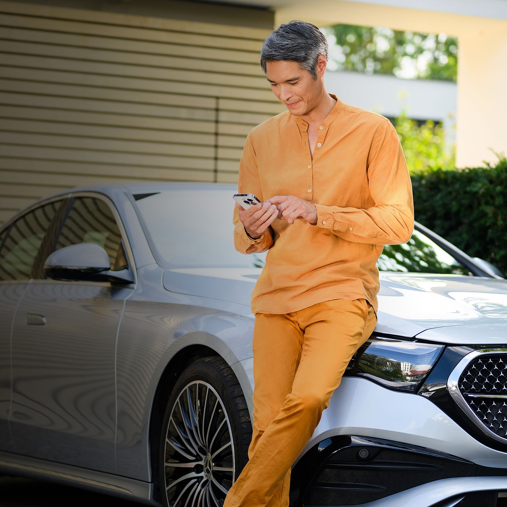 Osoba opřená o vozidlo Mercedes-Benz s mobilním telefonem.