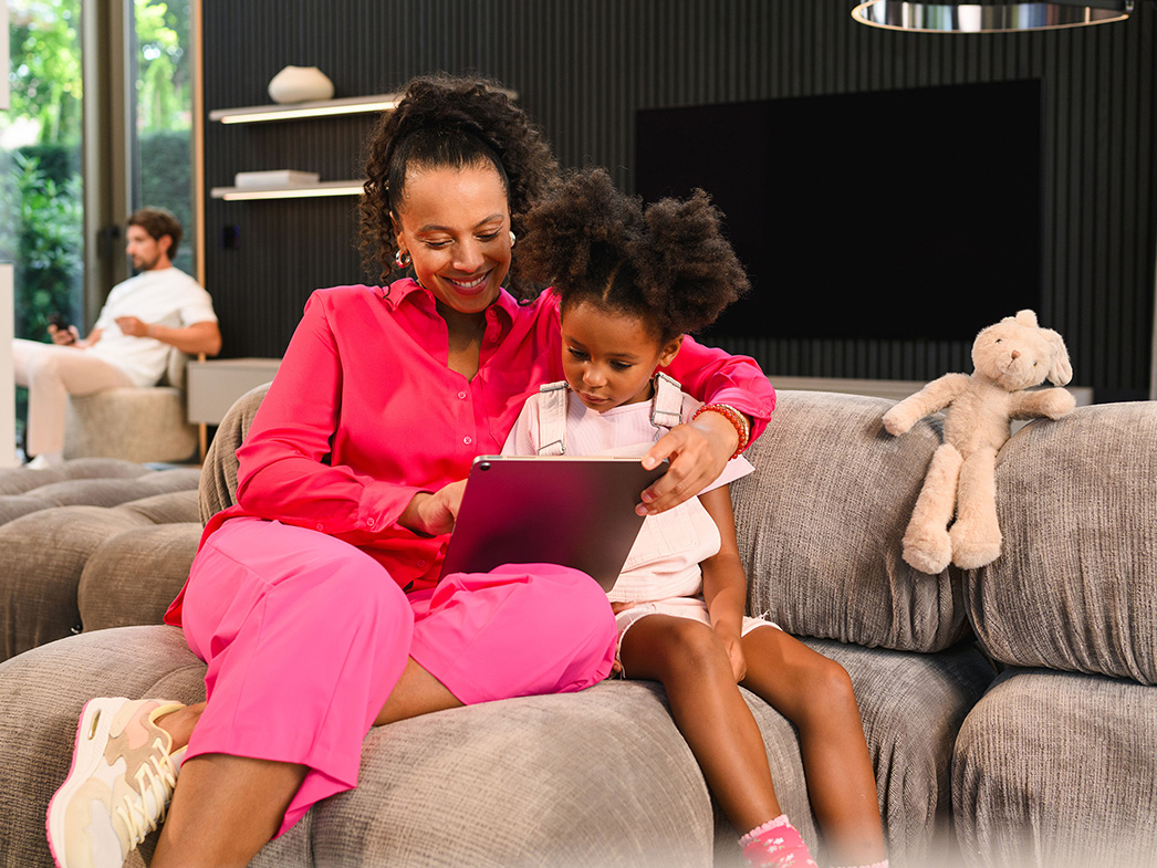 Přehled financování | Zákaznický portál Osoba a dítě sedí na pohovce s mobilním koncovým zařízením a další osoba sedí v dálce.