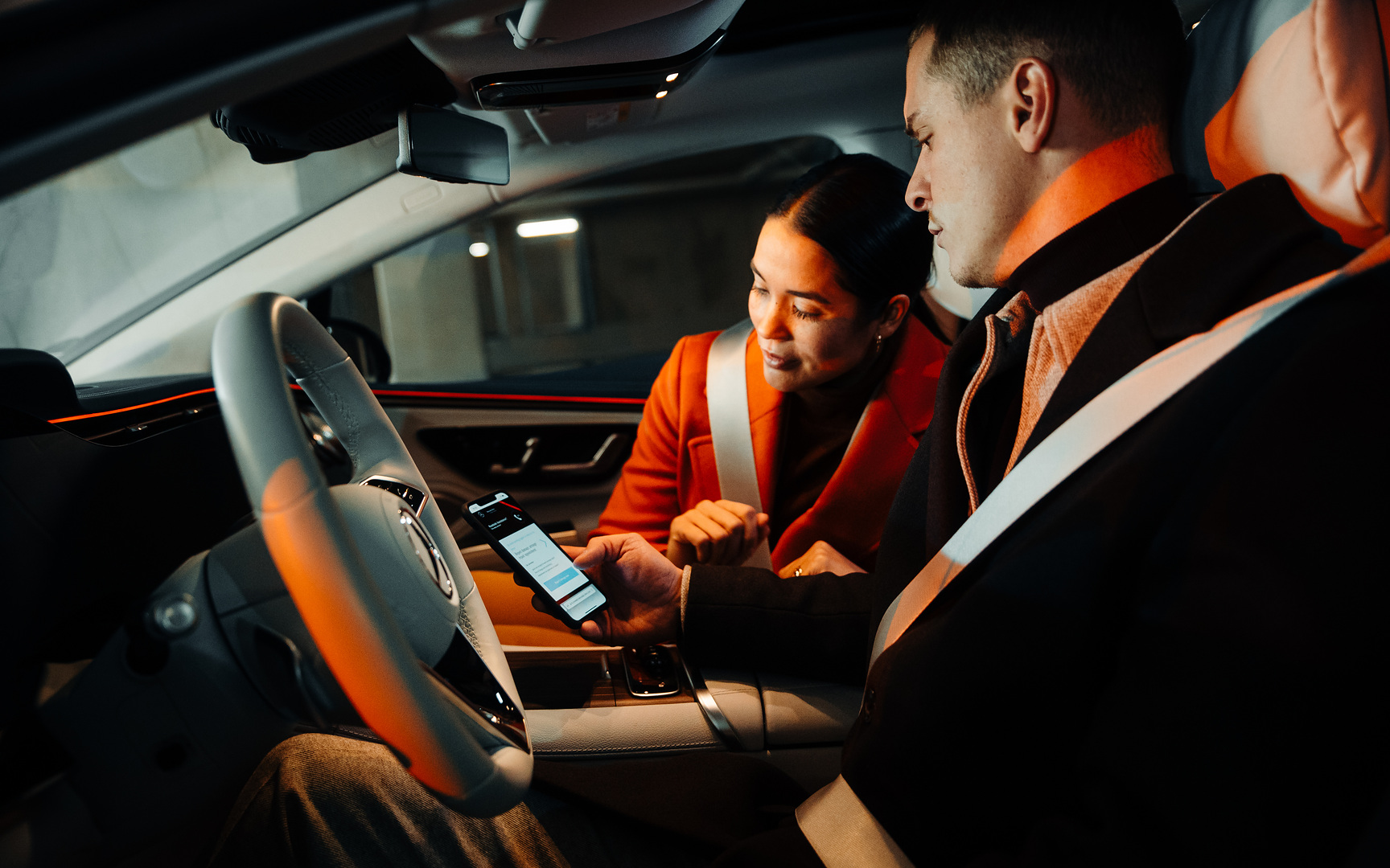 Ein Paar schaut, im Mercedes sitzend, gemeinsam auf ein Smartphone. Nahlásit poškození online. | Mercedes-Benz