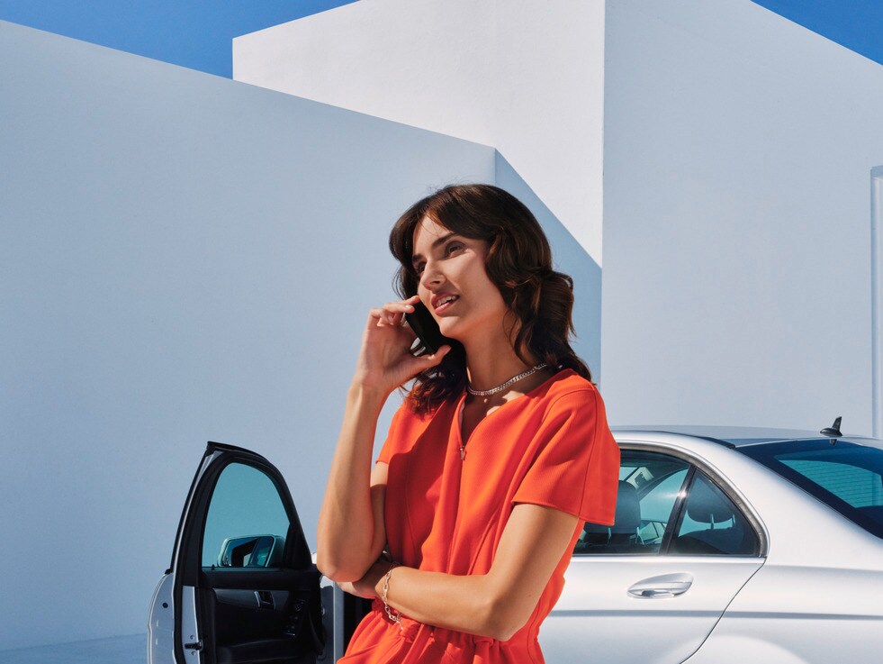 Žena telefonující před svým vozidlem Mercedes