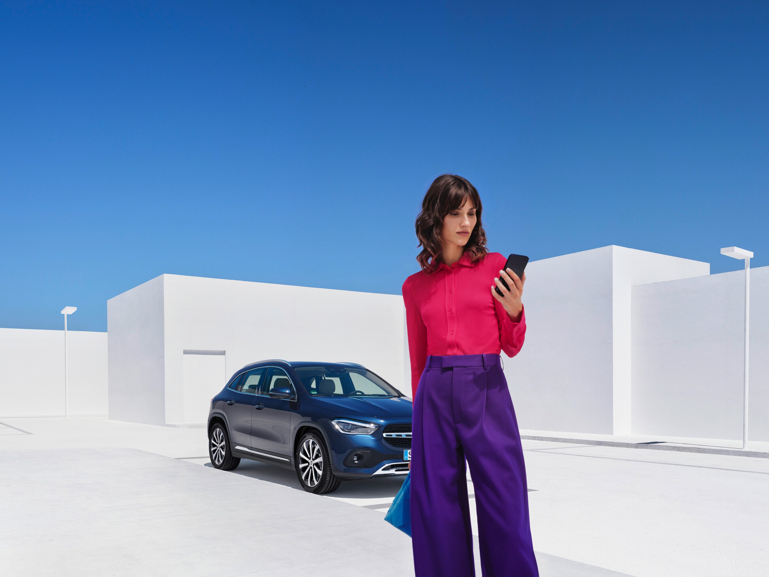 Žena stojí se svým chytrým telefonem před svým vozem Mercedes-Benz.