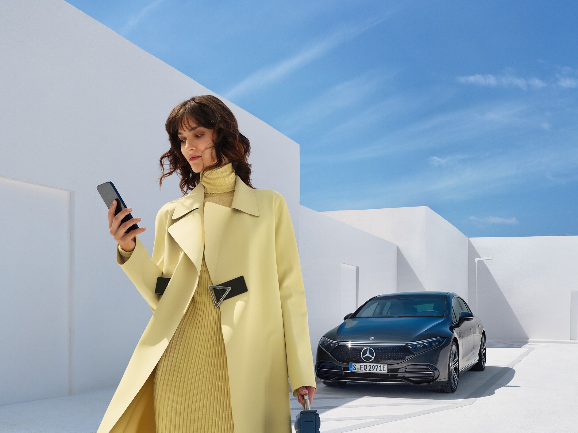 Žena se dívá na svůj mobilní telefon, když odchází od svého vozidla Mercedes-Benz s technologií EQ.