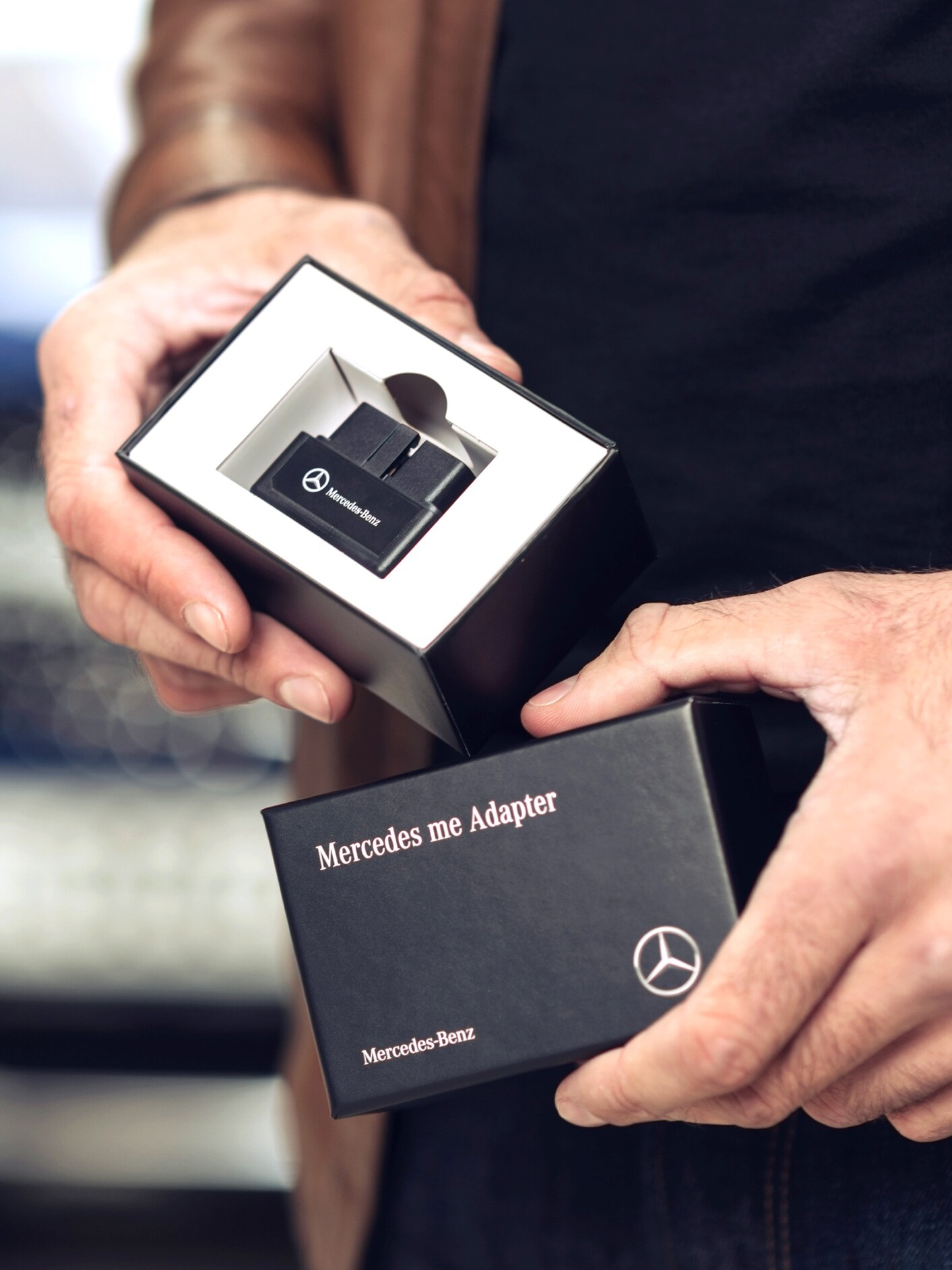 Muž vybaluje produkt Mercedes-Benz Adapter pro svůj vůz Mercedes-Benz, aby mohl využívat digitální doplňky ve svém vozidle.