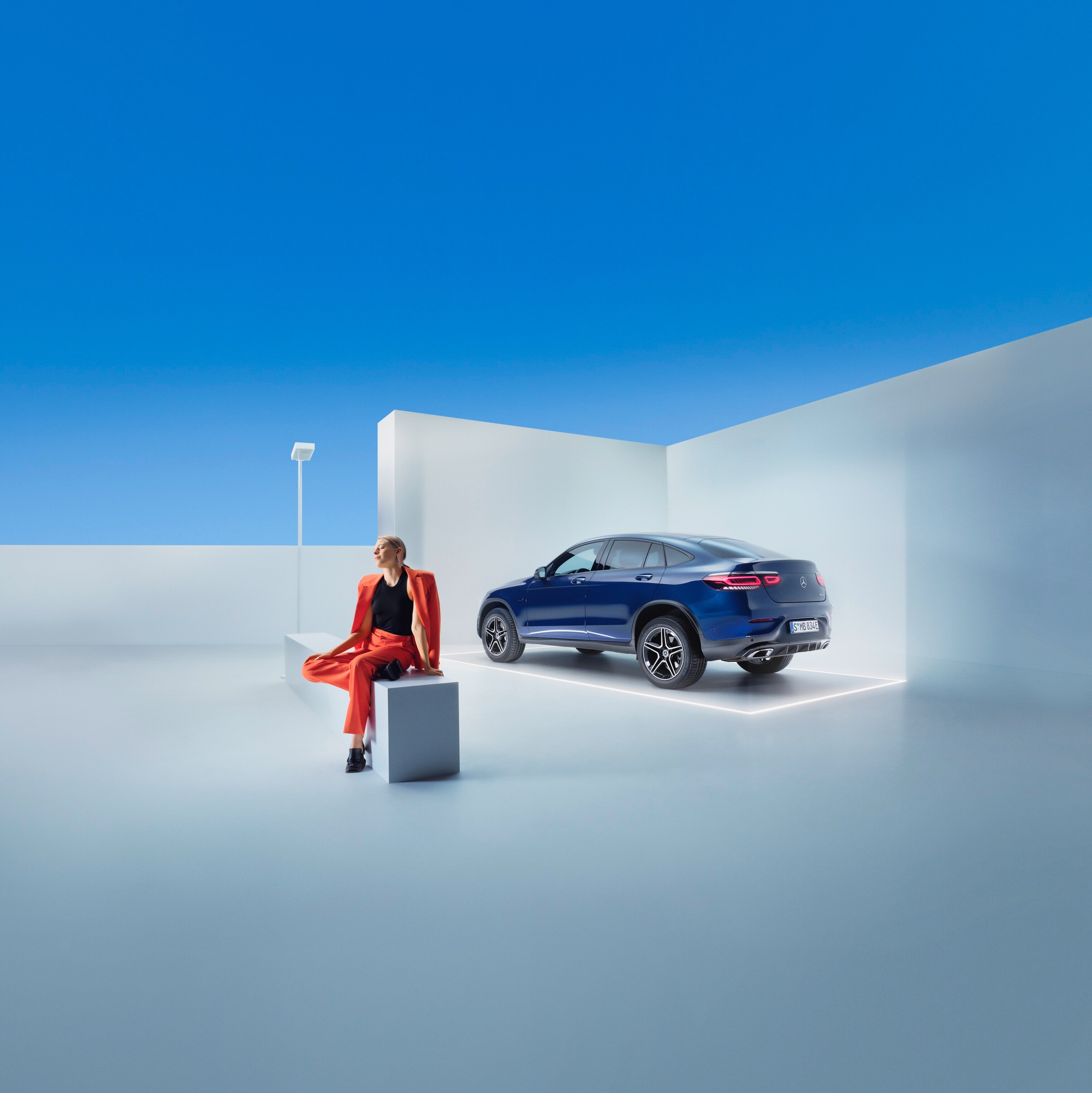 Žena sedí na lavici před vozem Mercedes-Benz.