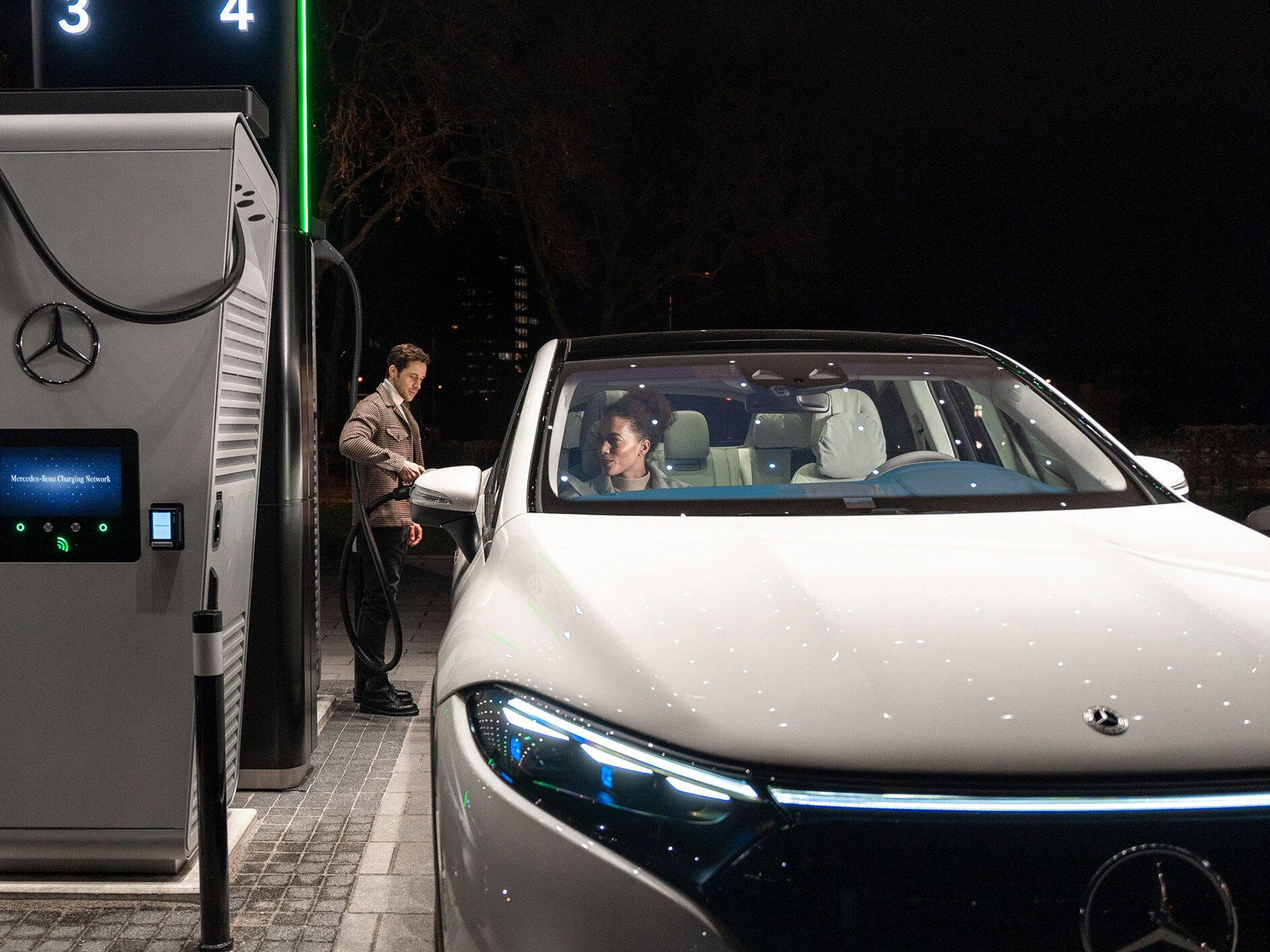 Osoba nabíjející vozidlo Mercedes-Benz EQS SUV na nabíjecí stanici.