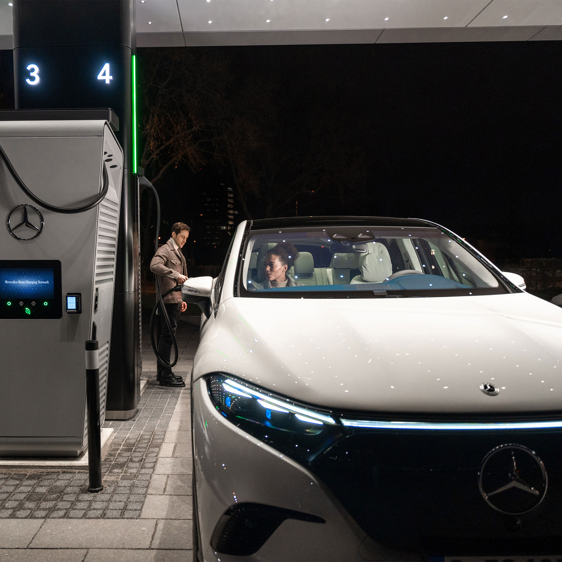 Nabíjení na veřejných stanicích | Nabíjení | Mercedes-Benz Osoba nabíjející vozidlo Mercedes-Benz EQS SUV na nabíjecí stanici.