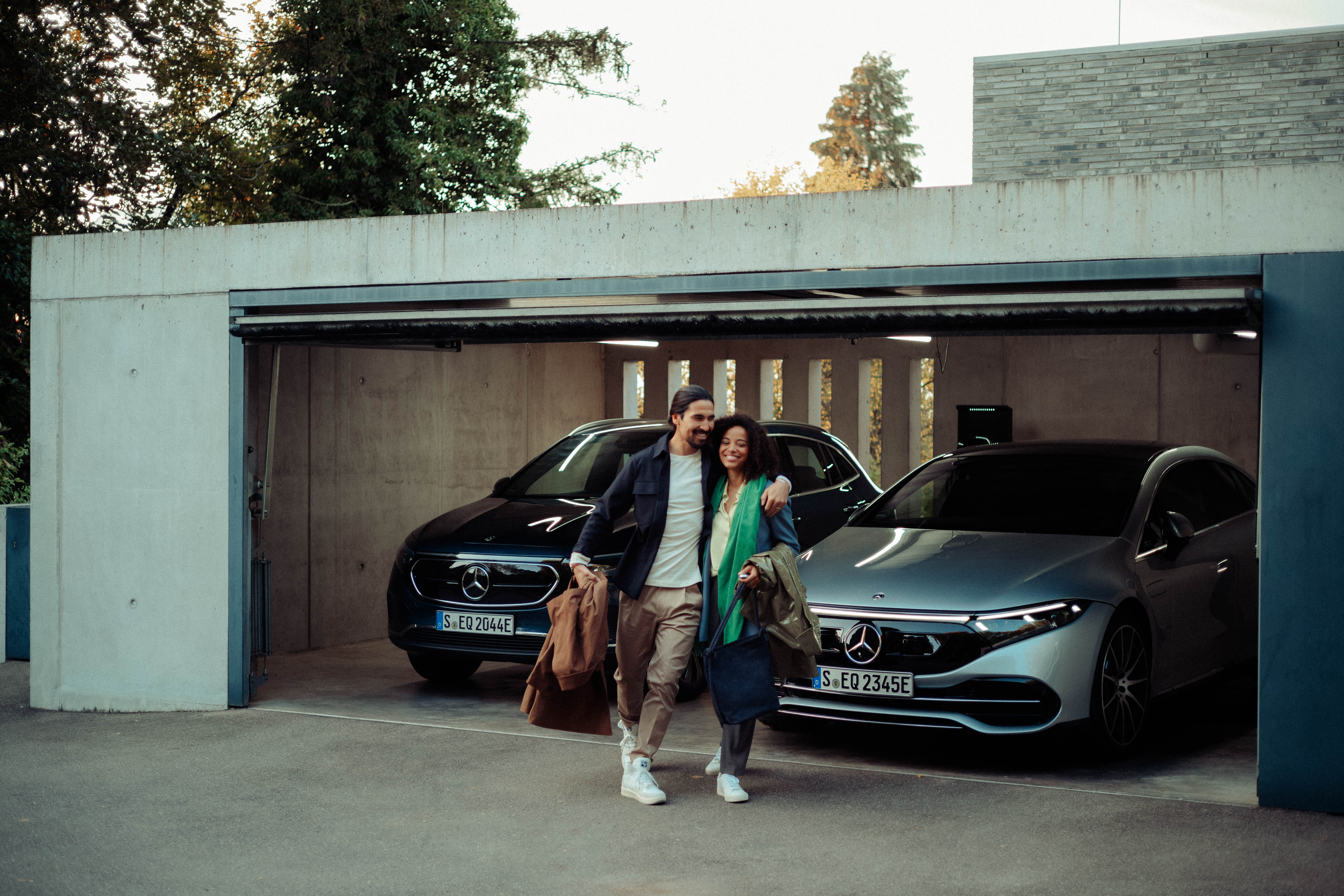 Aktivní parkovací asistent od Mercedes-Benz Žena a muž vyjíždějící z garáže, ve které byl zaparkován sedan EQS a EQA.