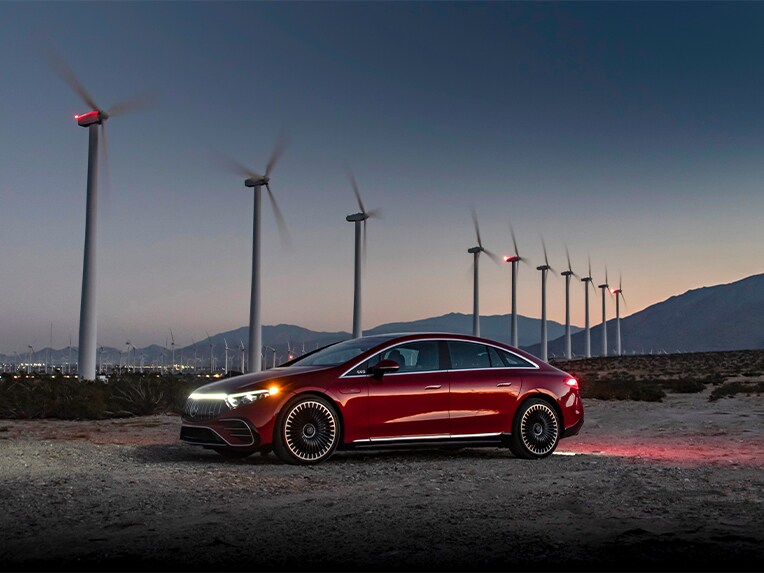 Červené vozidlo Mercedes-Benz EQS (V 297) zaparkované před větrnými mlýny.