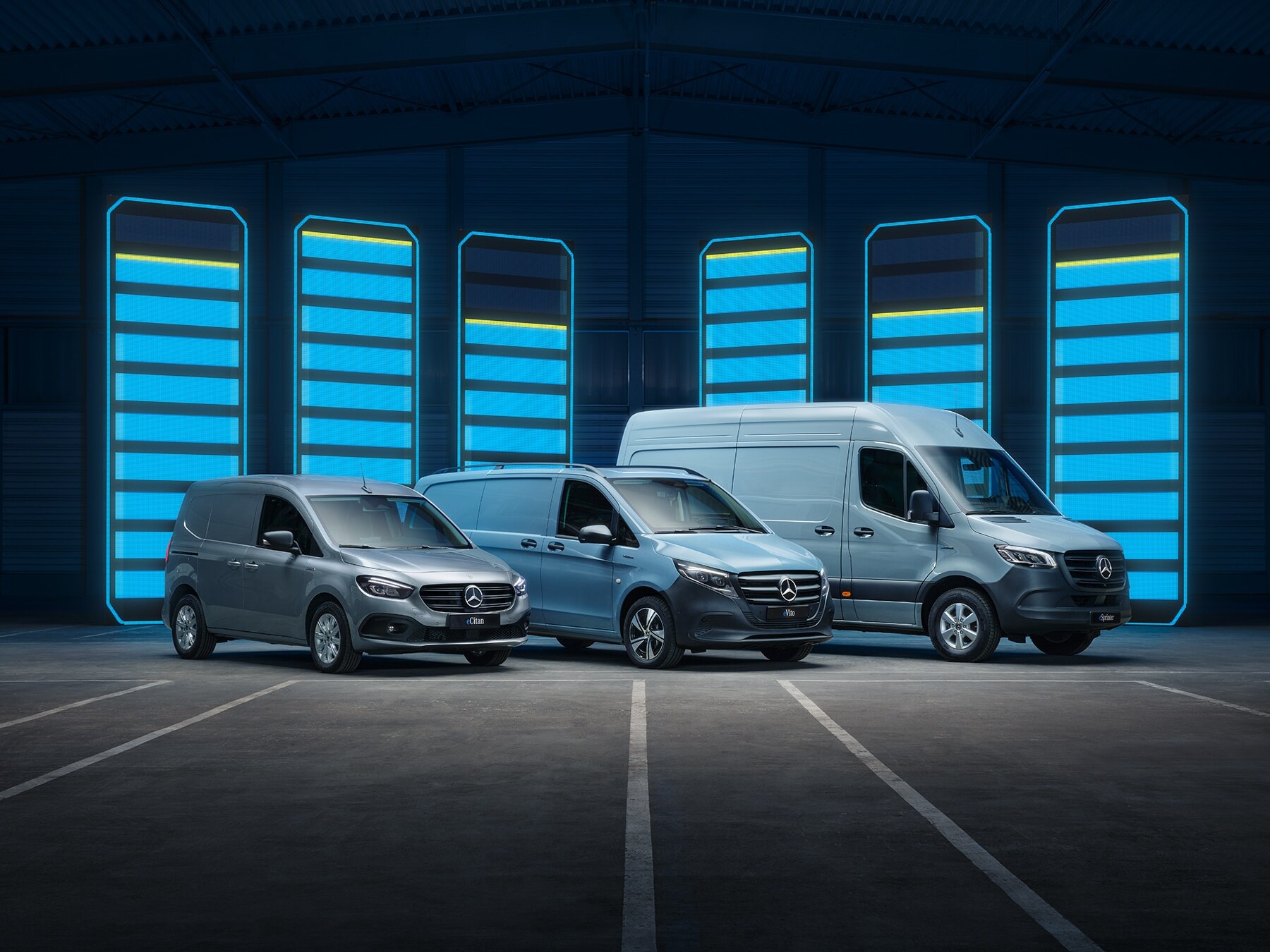 Modelová řada elektrických dodávkových vozidel Mercedes-Benz vystavená ve futuristickém skladu s&nbsp;osvětlenými nabíjecími lištami