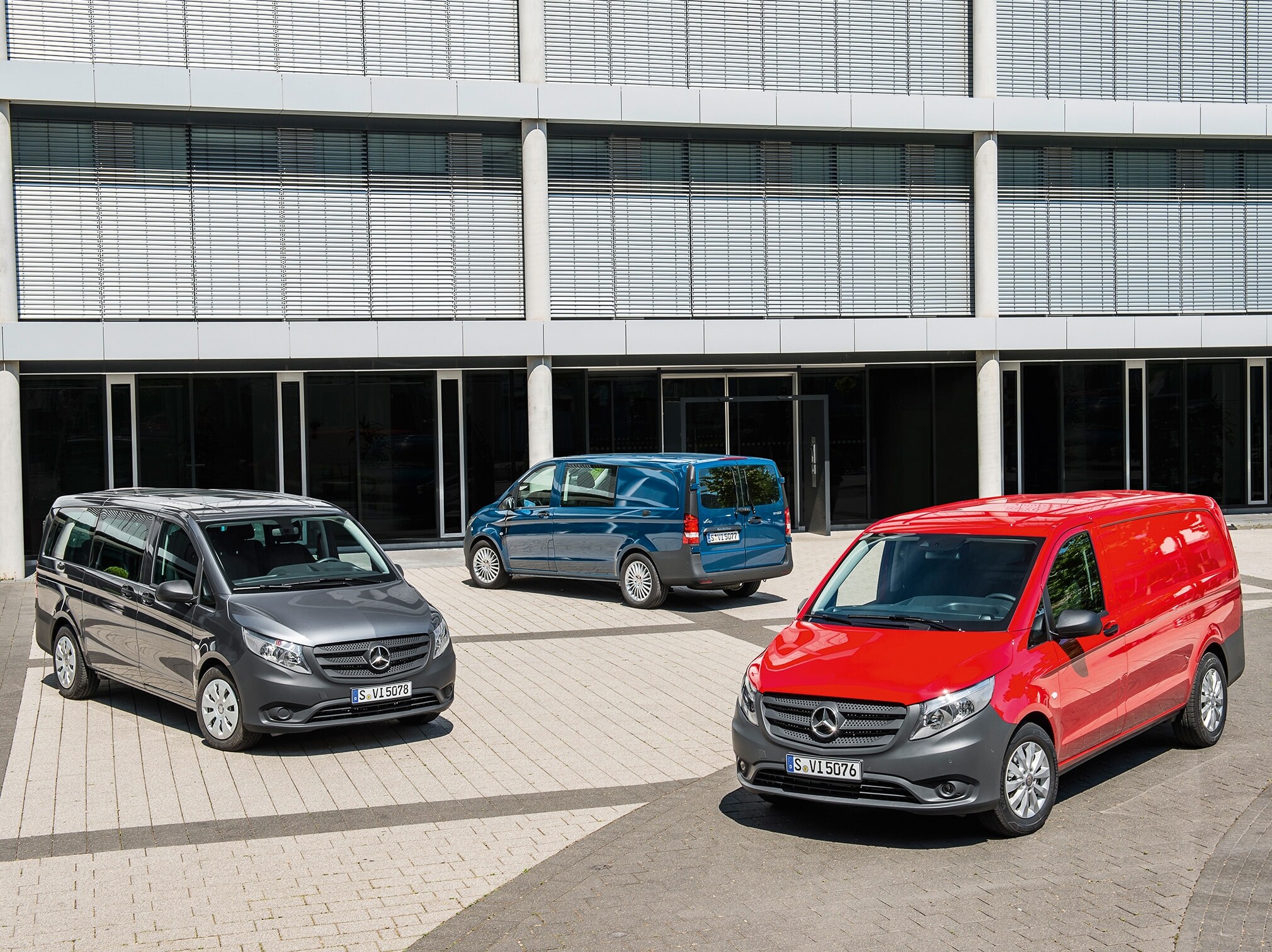 Několik vozů Mercedes-Benz Vito zaparkovaných před moderní kancelářskou budovou
