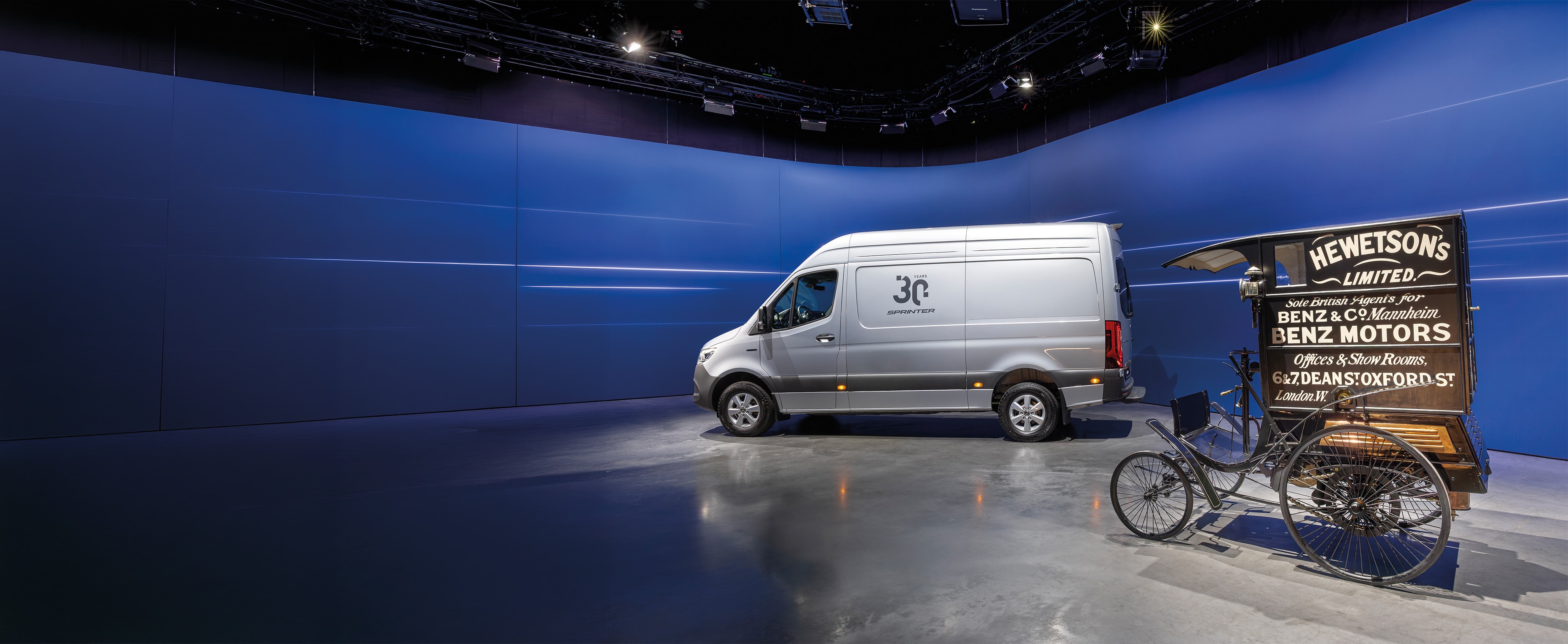 Historie | Užitková vozidla | Mercedes-Benz Dodávkové vozidlo Mercedes-Benz Sprinter a historické distribuční dodávkové vozidlo Benz vystavené v moderním showroomu