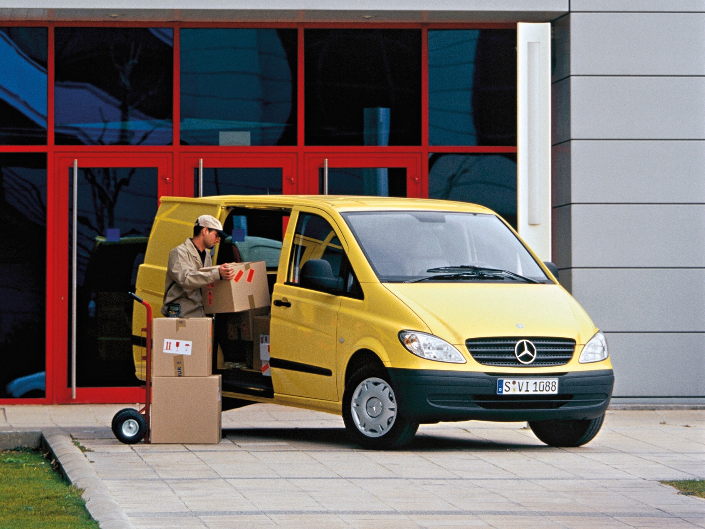 Žlutý vůz Mercedes-Benz Vito zaparkovaný před budovou s&nbsp;pracovníkem, který vykládá balíky