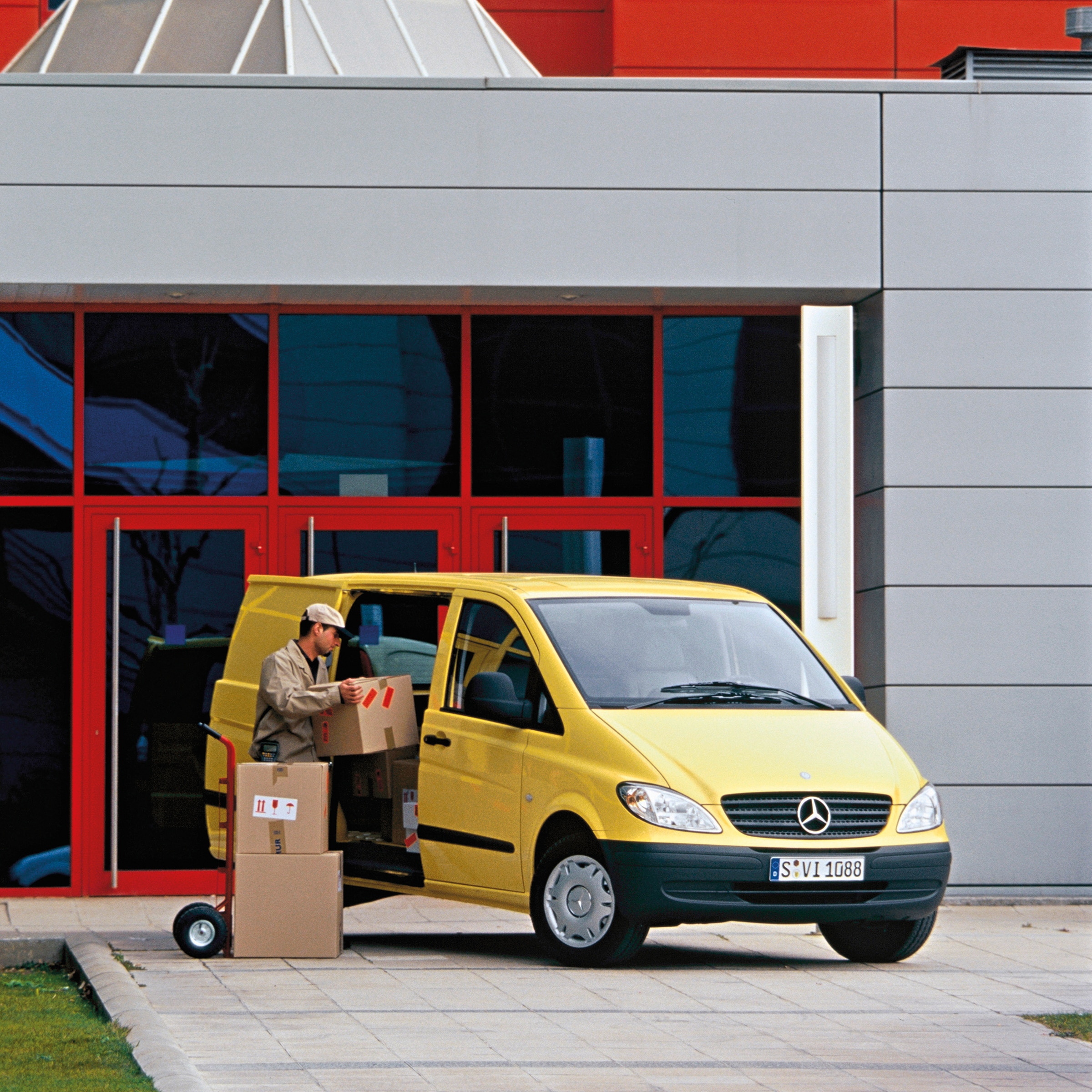 Druhá generace vozidel Mercedes-Benz Vito | Historie užitkových vozidel | Mercedes-Benz Žlutý vůz Mercedes-Benz Vito zaparkovaný před budovou s pracovníkem, který vykládá balíky