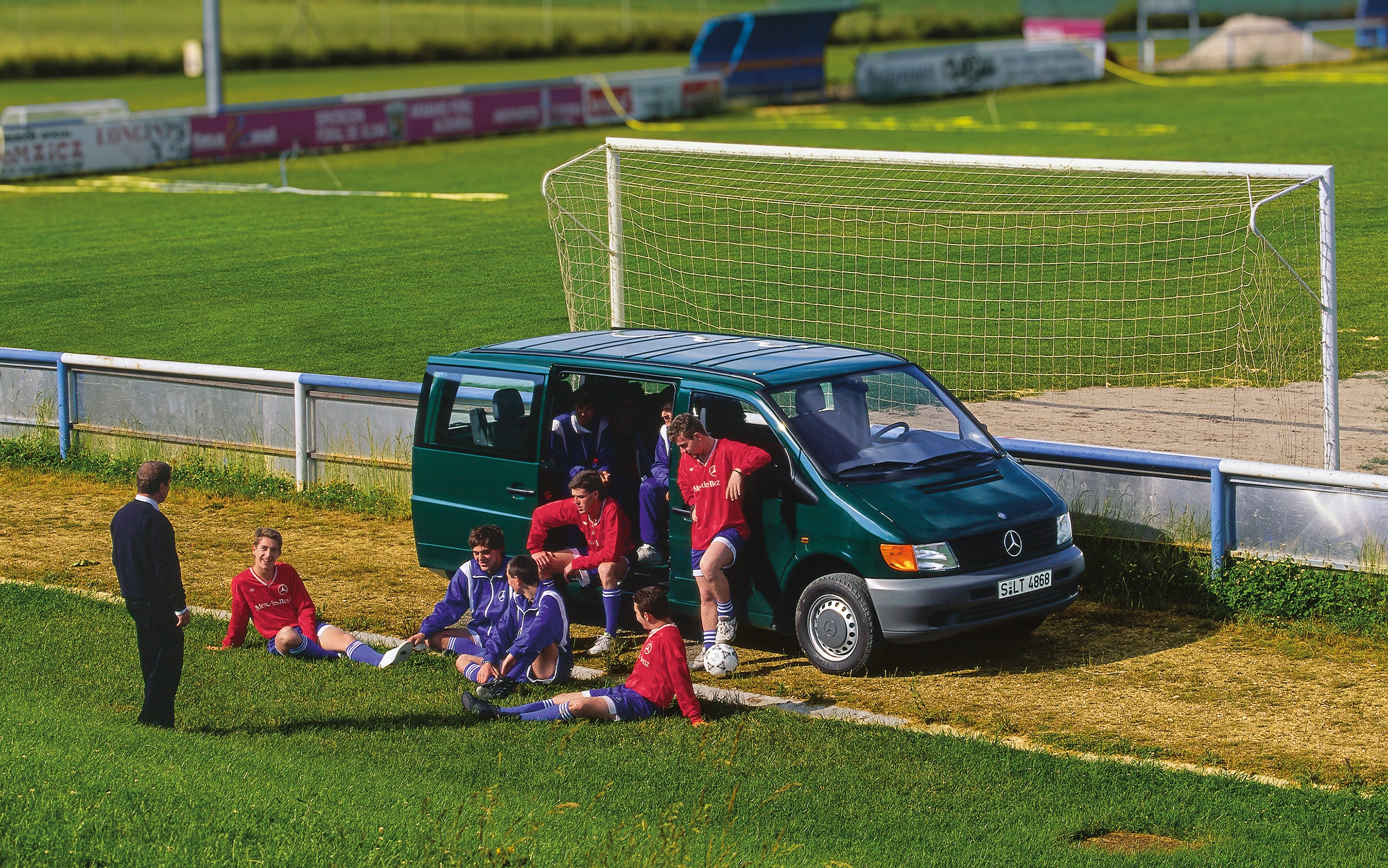 První generace vozidel Mercedes-Benz Vito | Historie užitkových vozidel | Mercedes-Benz Vito první generace zaparkované vedle fotbalového hřiště s hráči týmu poblíž
