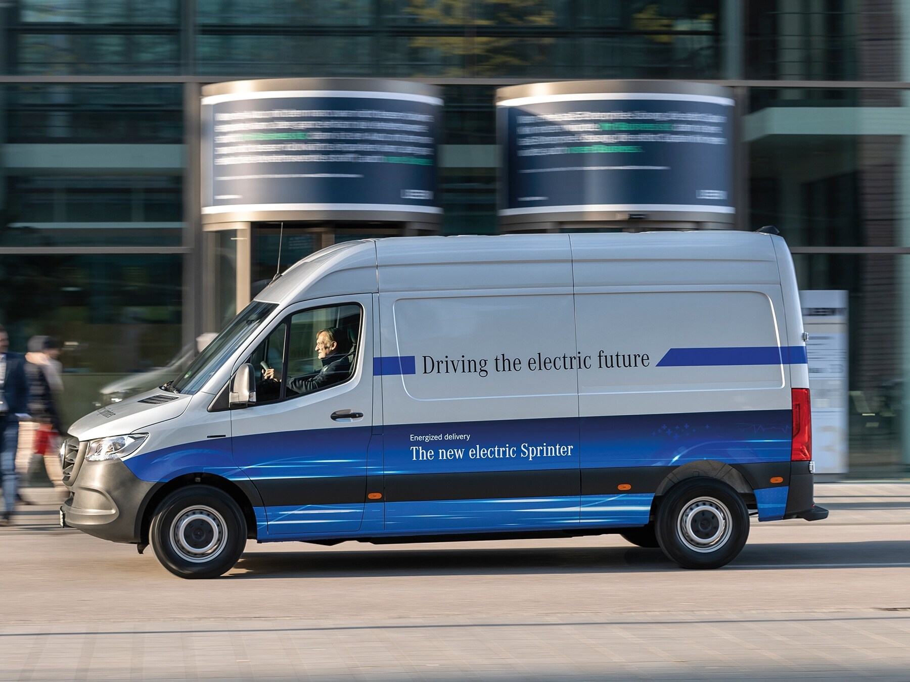 Skříňová dodávka Mercedes-Benz eSprinter projíždějící moderní městskou ulicí