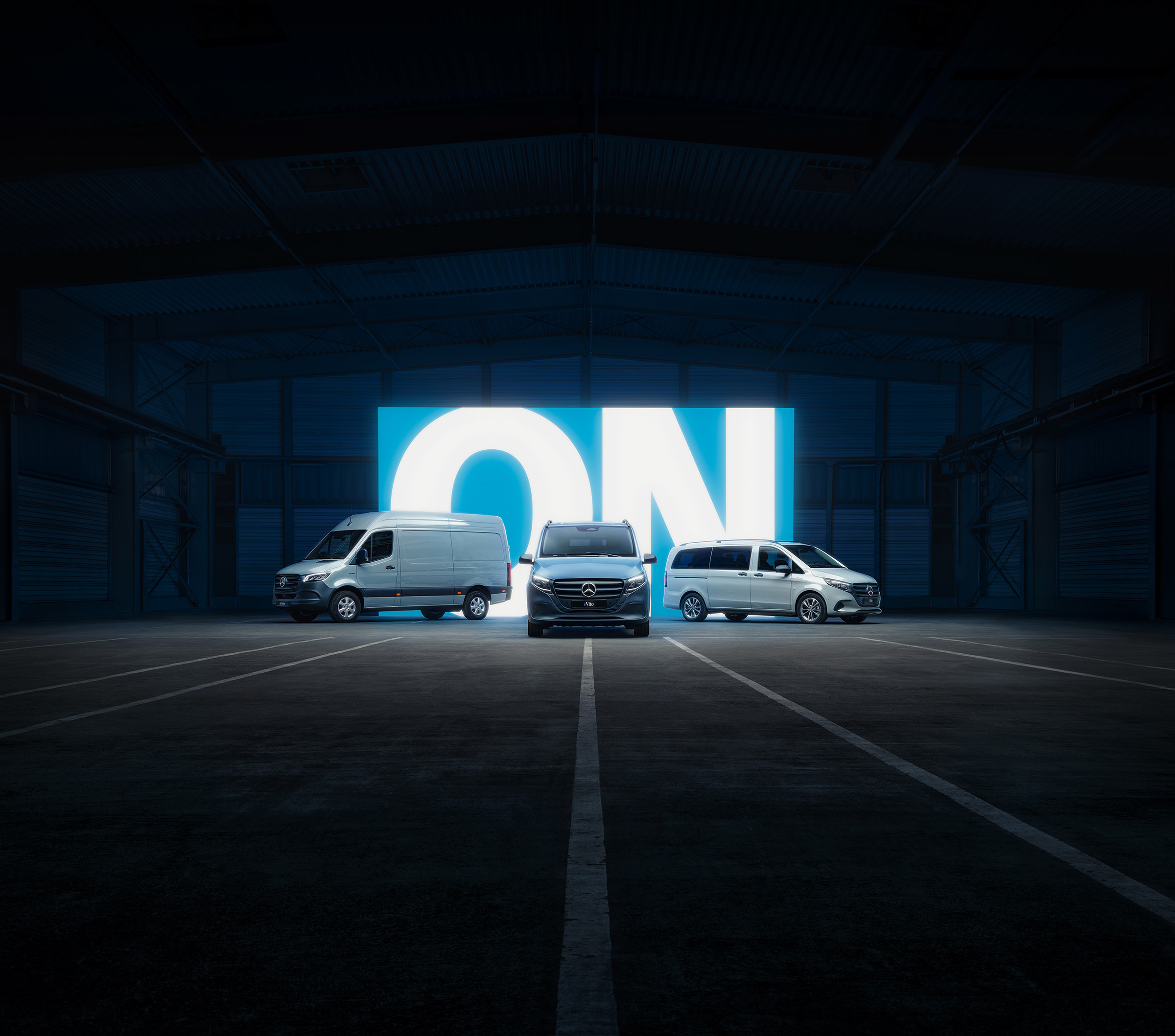 Elektrický dojezd | Všechny modely Sprinter | Dodávková vozidla Mercedes-Benz Řada elektrických dodávkových vozidel Mercedes-Benz s modely eSprinter a eVito v osvětleném showroomu.
