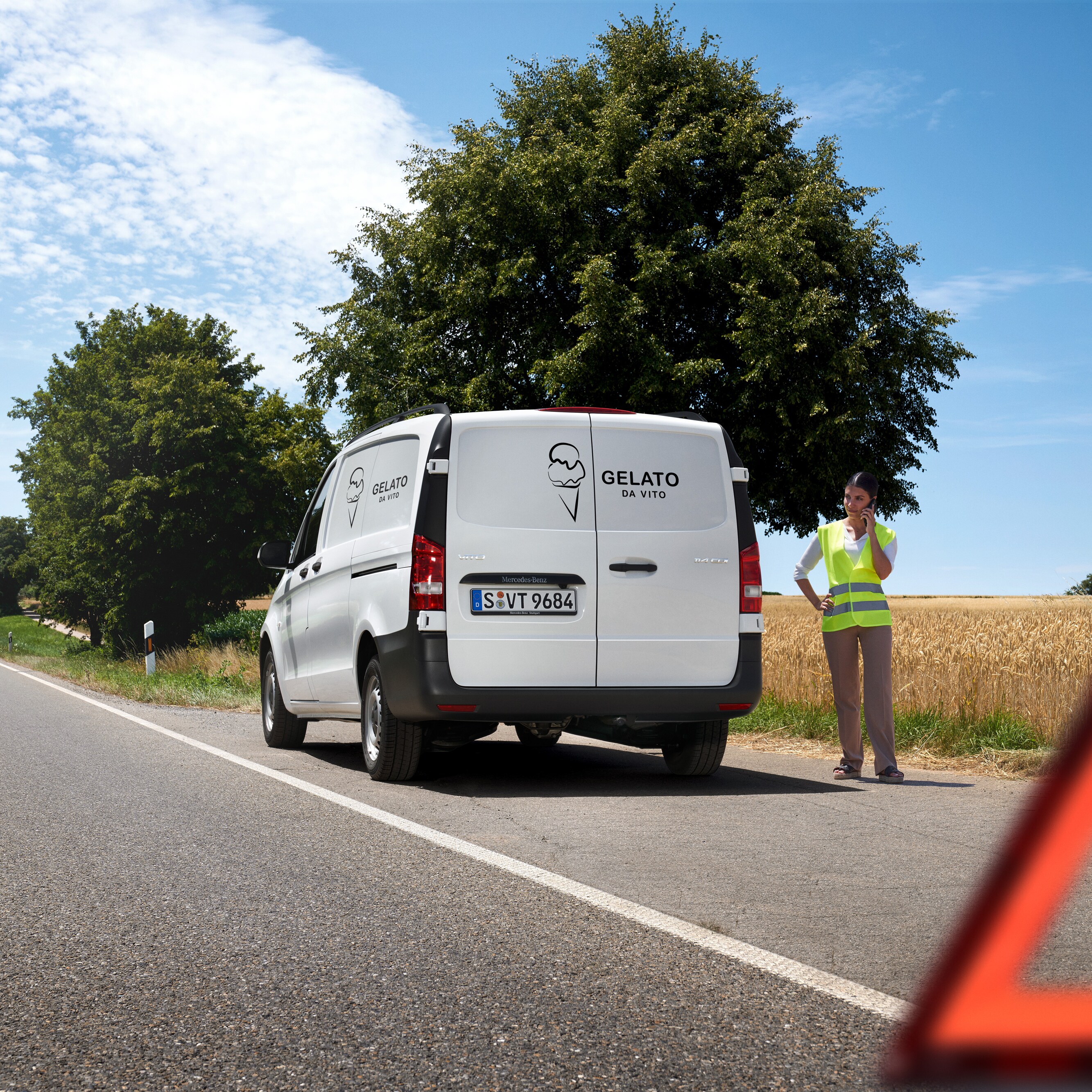Žena volá na servisní hotline Mercedes-Benz Service24h, u krajnice venkovské silnice stojí dodávka Mercedes-Benz Sprinter.