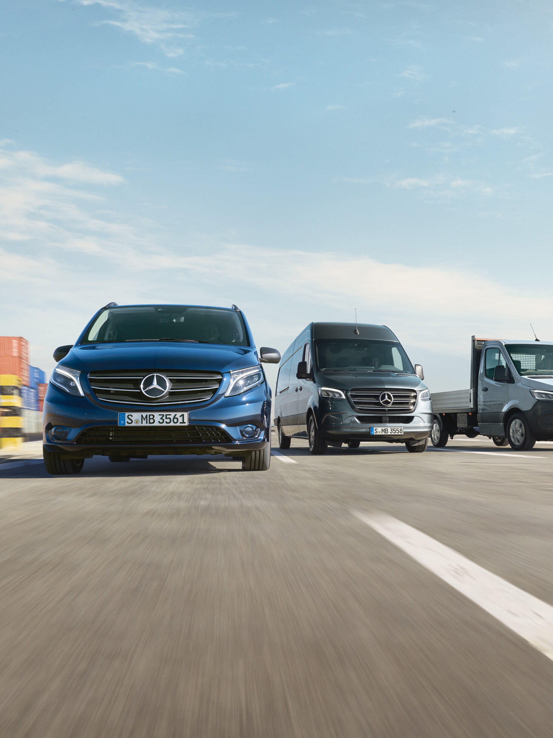 Řada dodávkových vozidel Mercedes-Benz zaparkovaných vedle sebe na silnici vedle nakládací rampy.