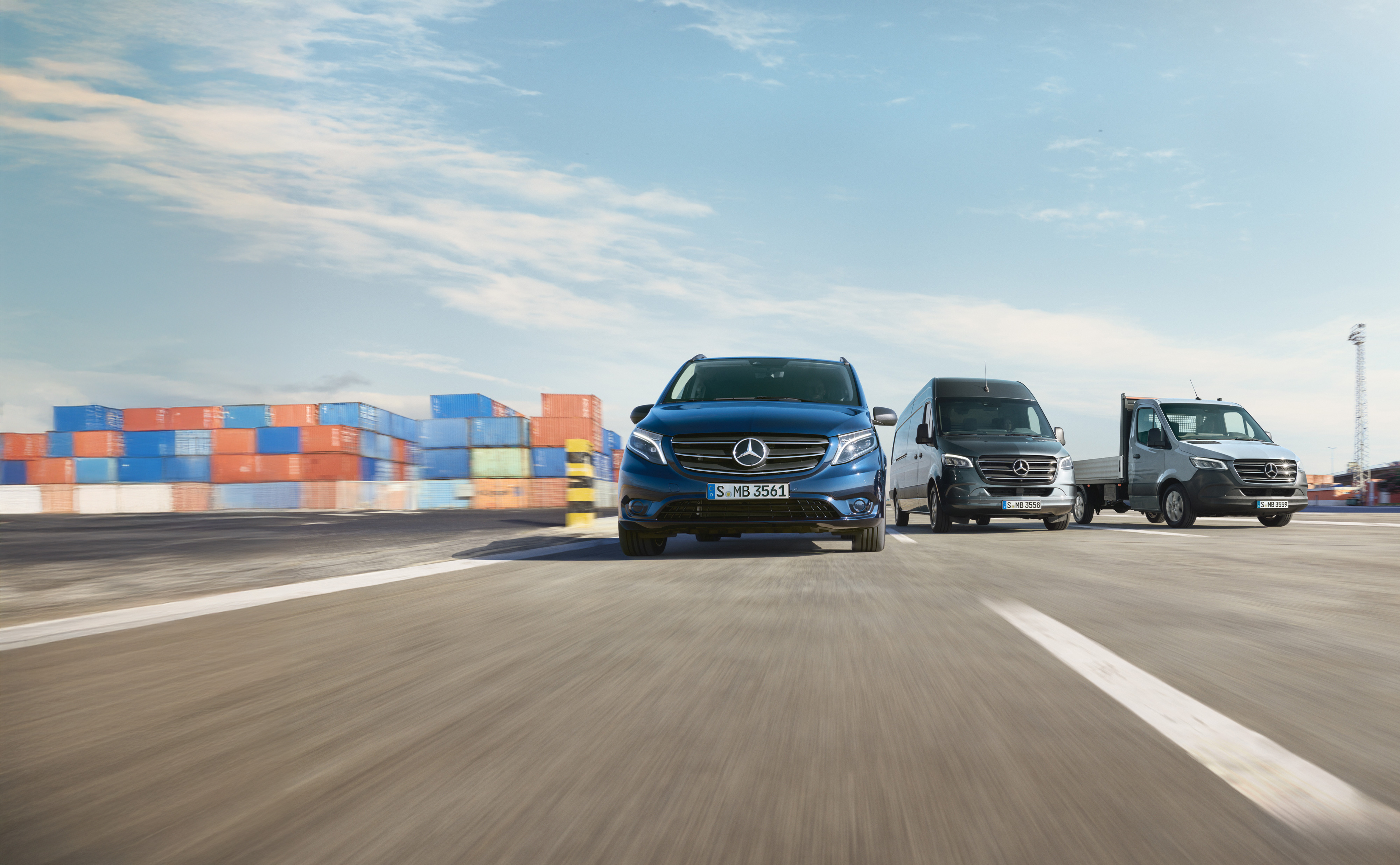 Mercedes-Benz | Vans Care | Service24h Řada dodávkových vozidel Mercedes-Benz zaparkovaných vedle sebe na silnici vedle nakládací rampy.