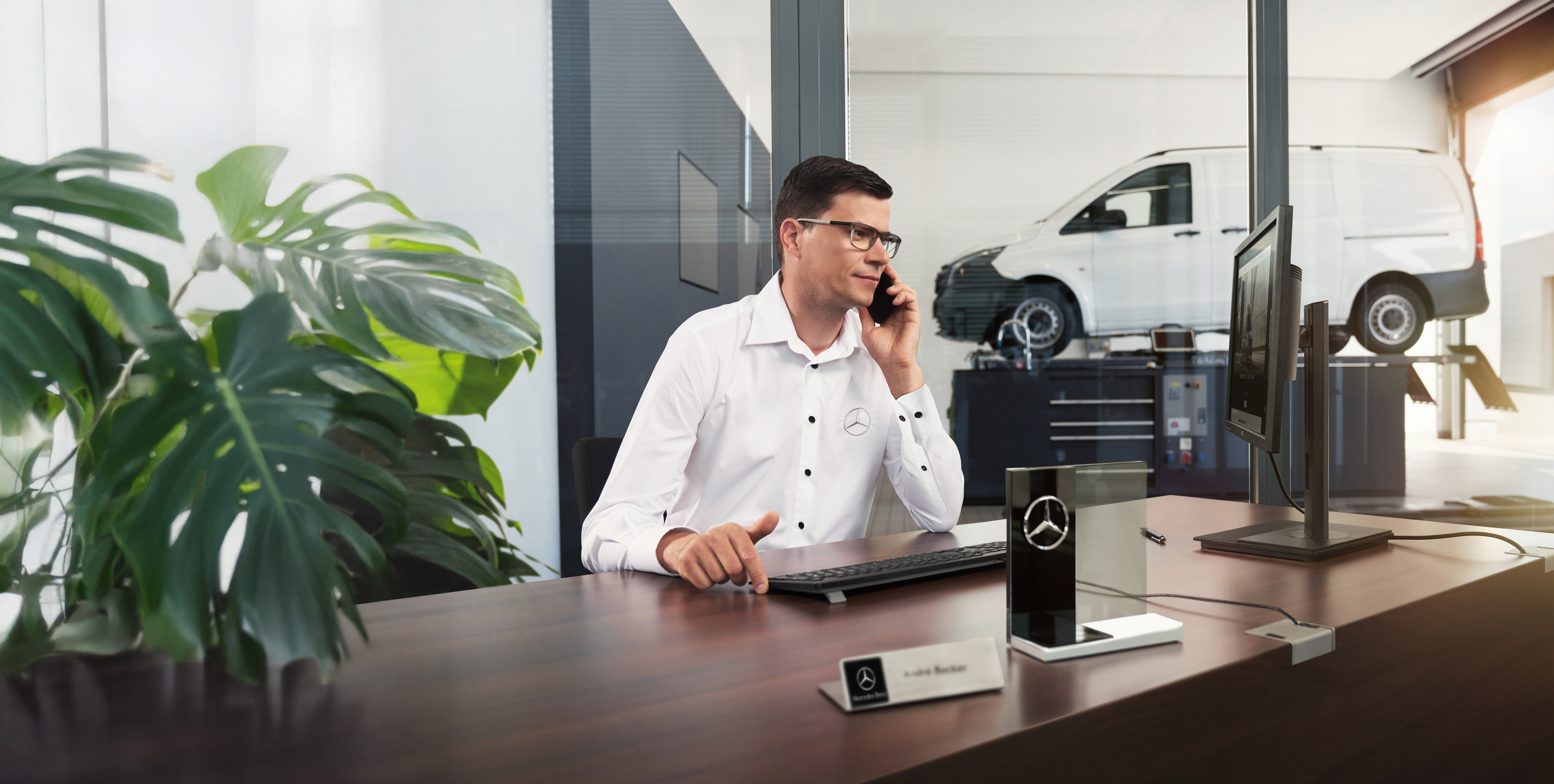 Mercedes-Benz | Vans Care Zaměstnanec Mercedes-Benz telefonuje u stolu, s dodávkovým vozidlem Mercedes-Benz Vito v dílně.