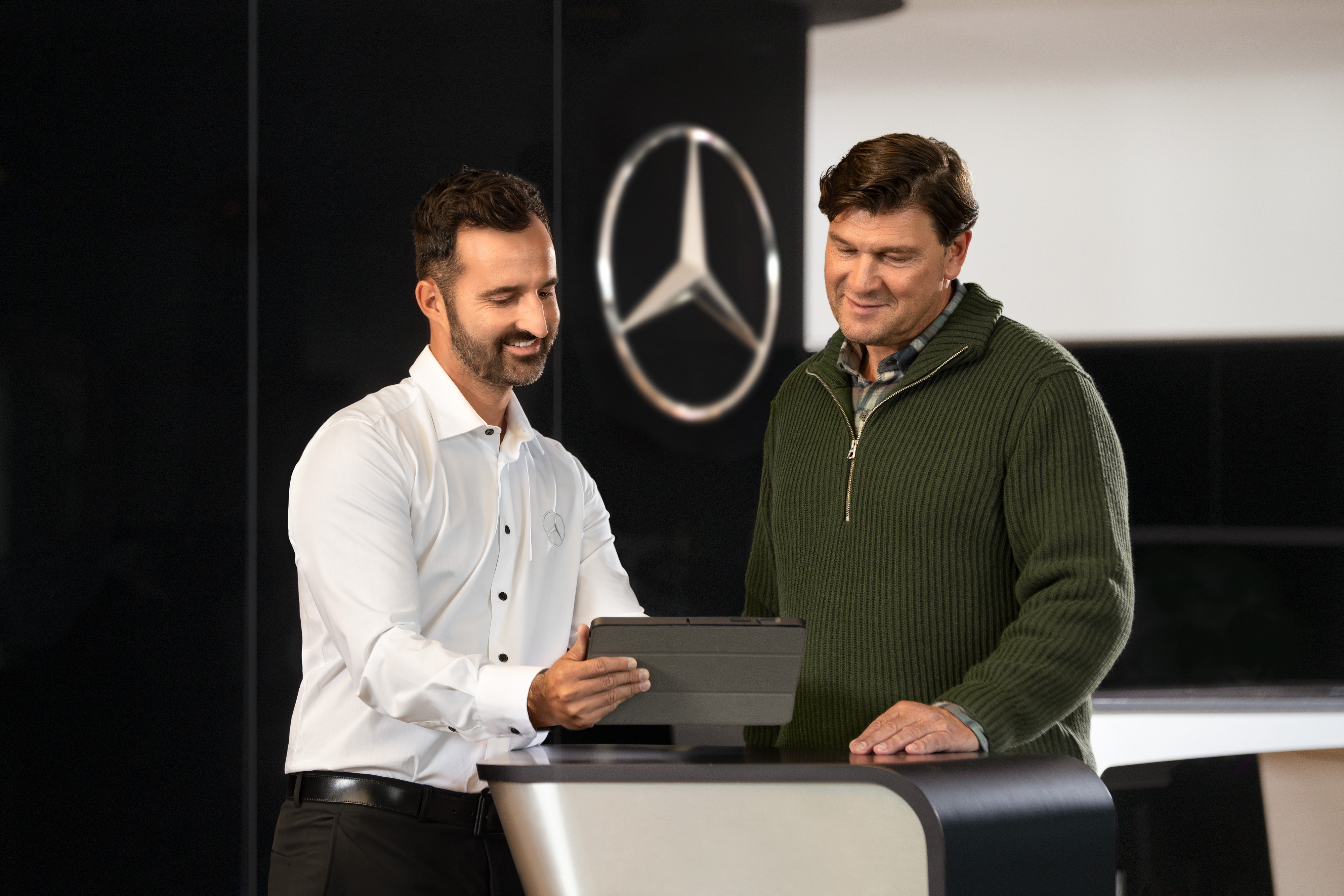 Mercedes-Benz | Péče o dodávkové vozidlo | Individuální podpora Zaměstnanec společnosti Mercedes radí zákazníkům u přepážky pomocí tabletu – individuální podpora a obchodní poradenství v autosalonu.