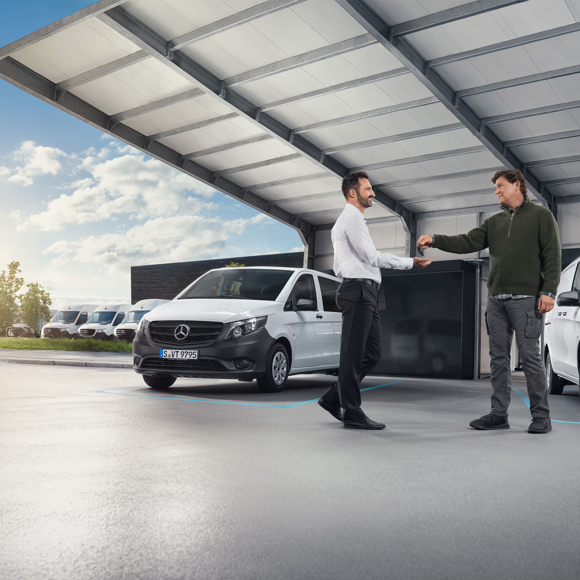 Dva muži diskutují před řadou bílých dodávek Mercedes-Benz v hale.