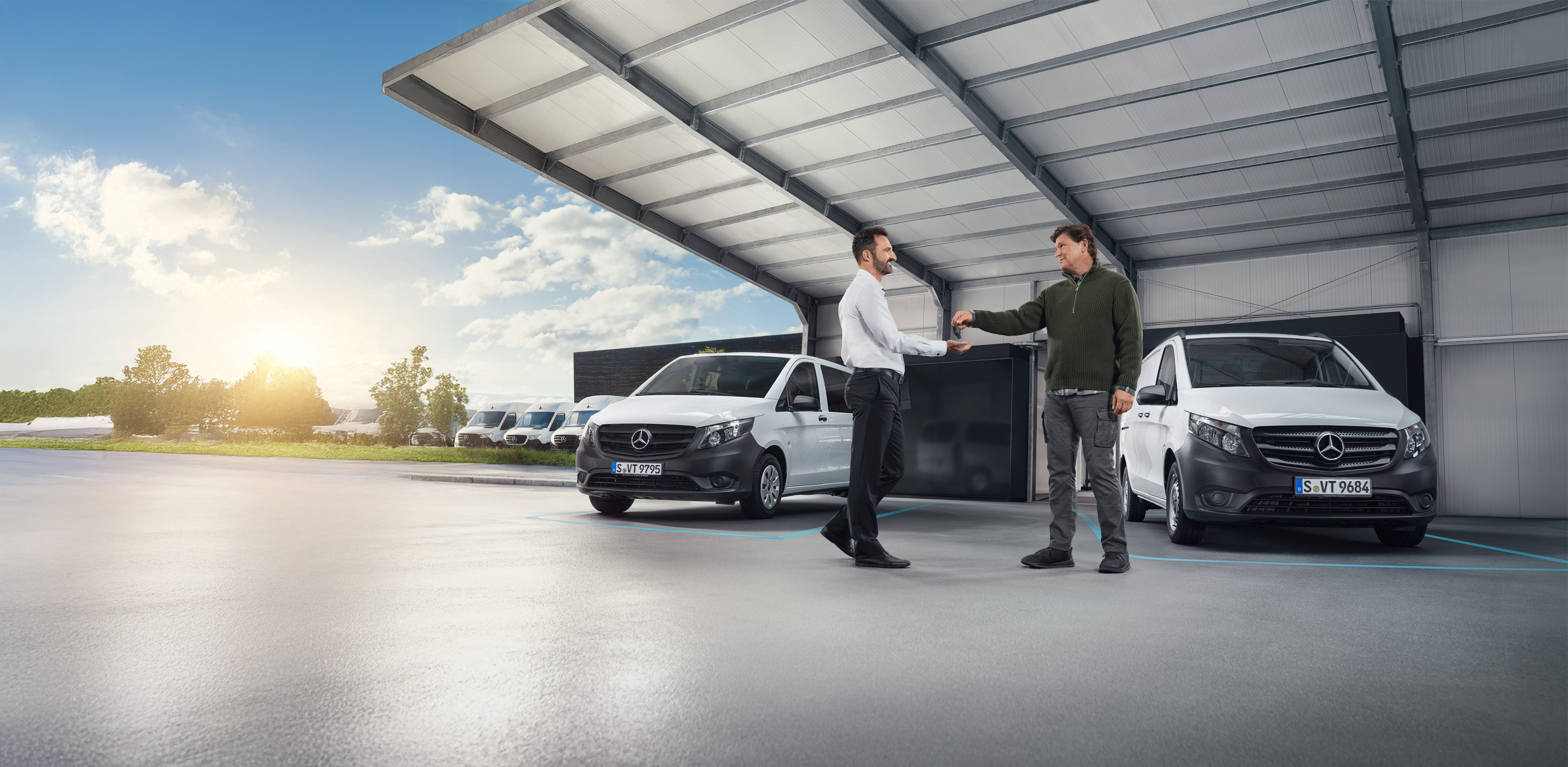 Mercedes-Benz | Péče o dodávky | Individuální podpora Dva muži diskutují před řadou bílých dodávek Mercedes-Benz v hale.