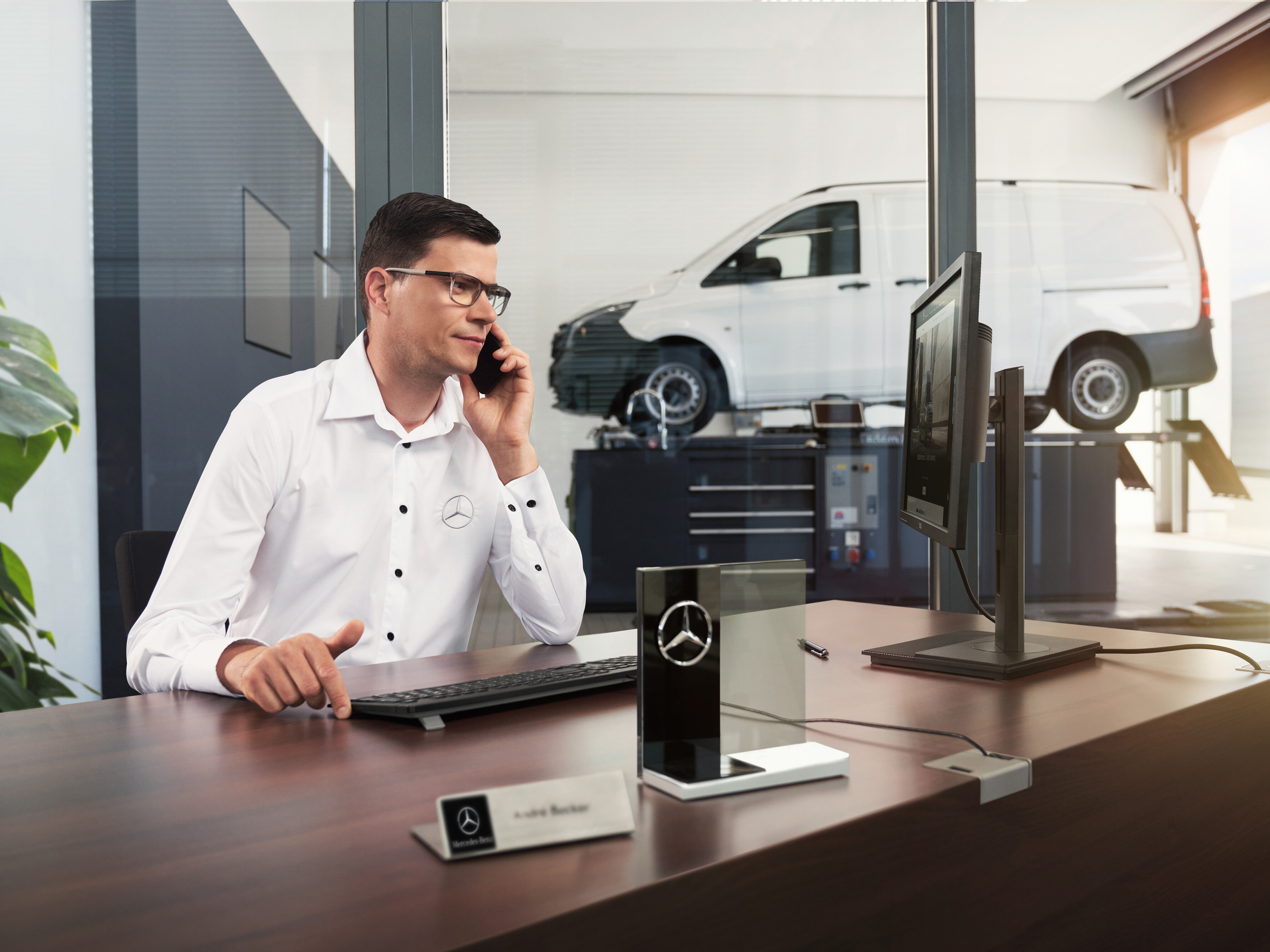 Přijímací technik Mercedes-Benz telefonuje v&nbsp;dílně.