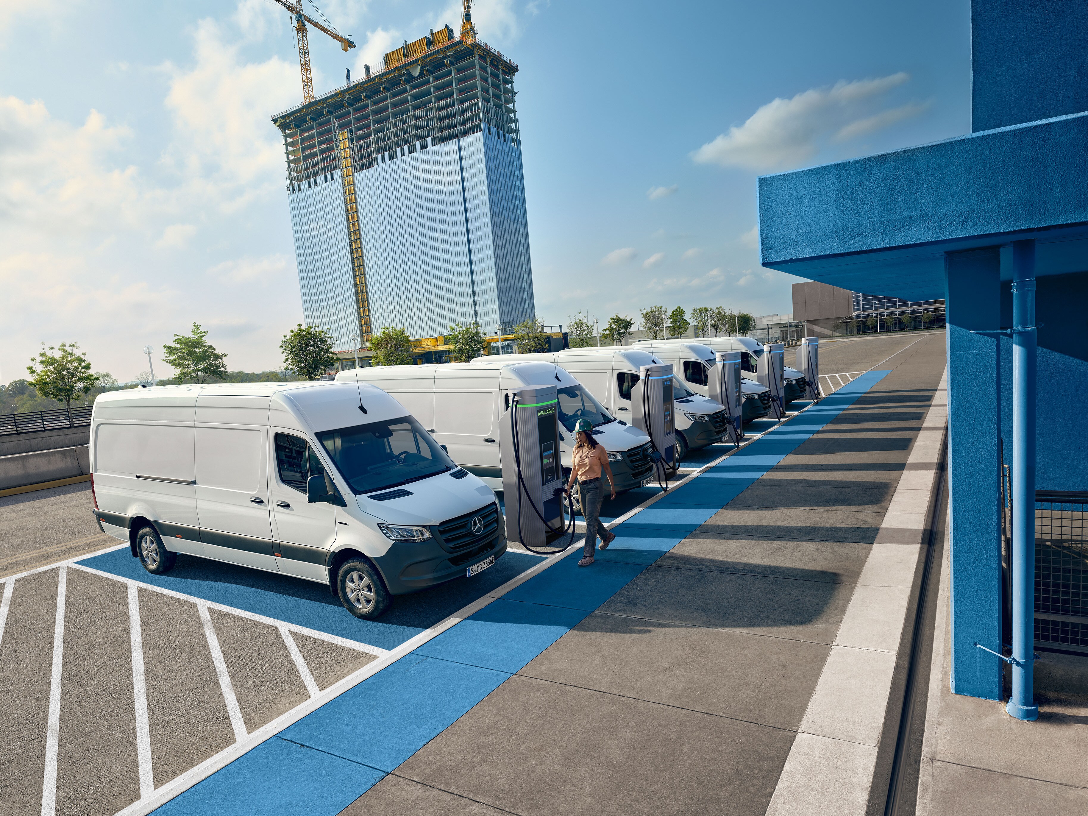 Vozový park bílých elektrických dodávek Mercedes-Benz zaparkovaných u&nbsp;nabíjecího centra.
