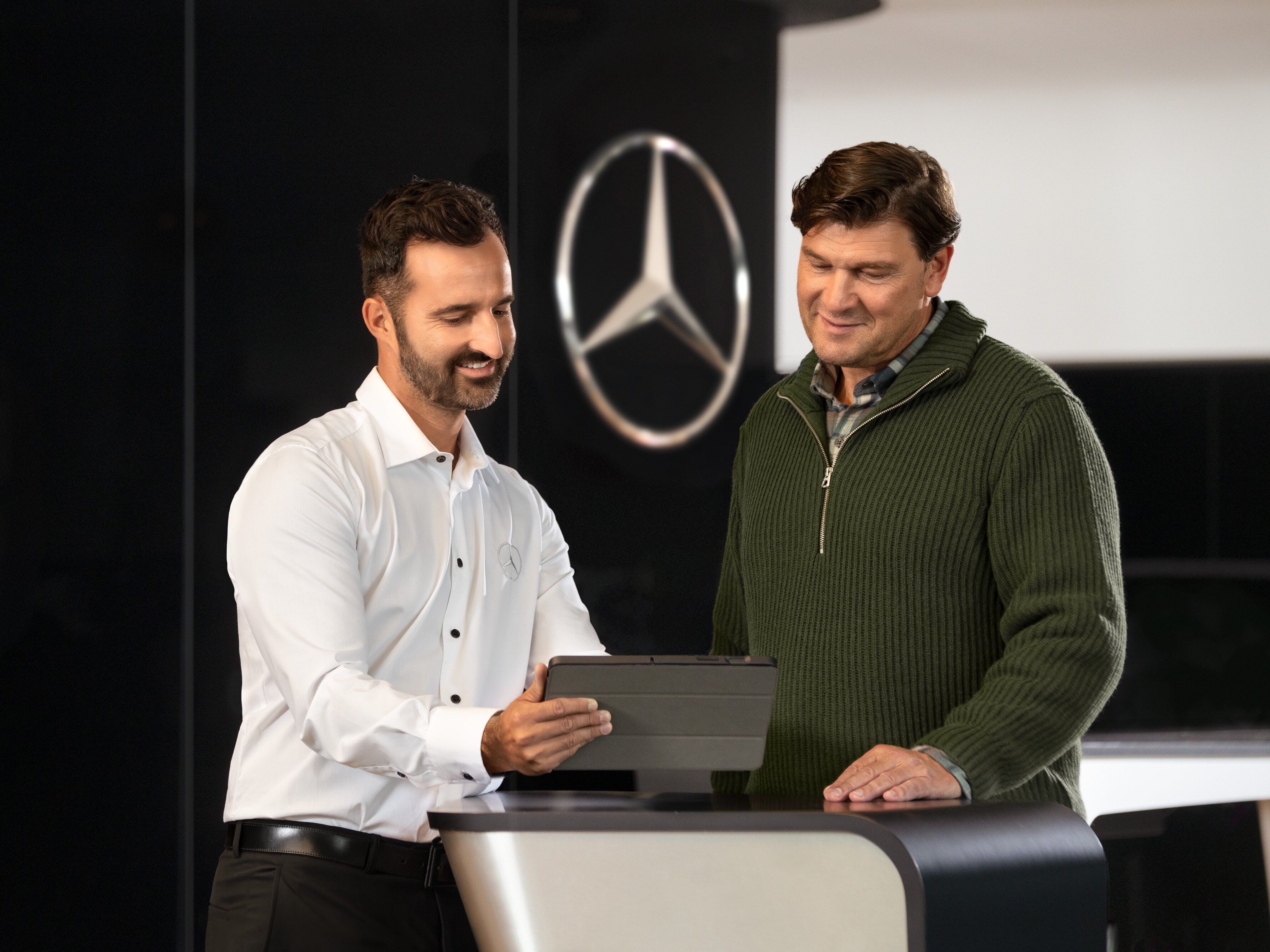Zaměstnanec Mercedes-Benz hovoří se zákazníkem a&nbsp;dívá se na tabletové zařízení.