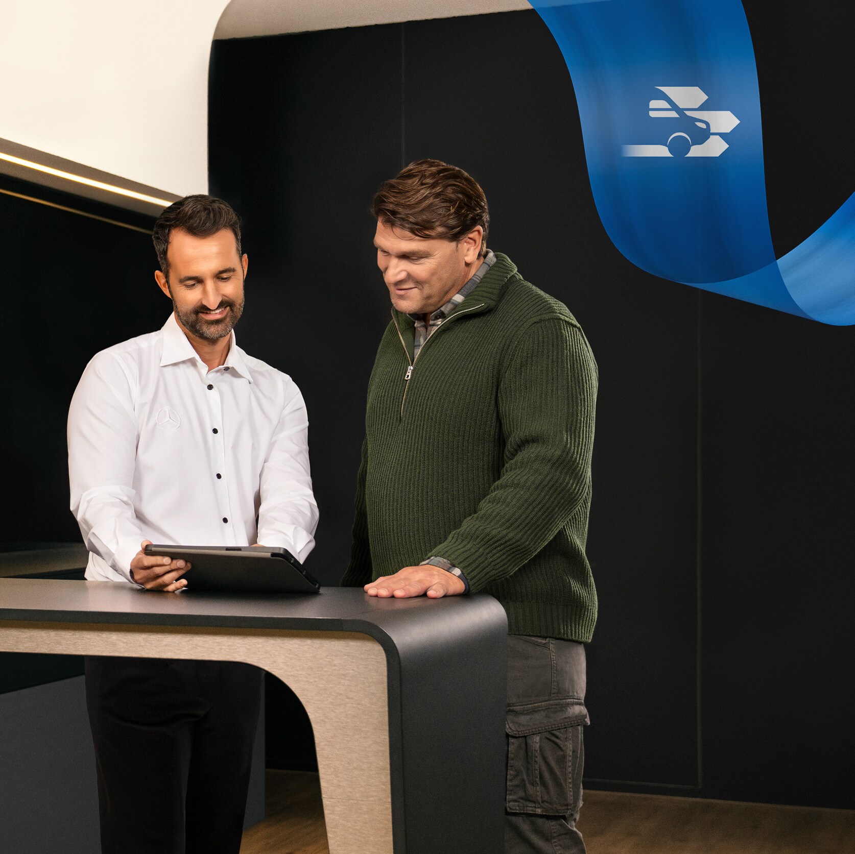 Dva muži stojící v&nbsp;kanceláři servisního partnera Mercedes-Benz a&nbsp;diskutující o&nbsp;něčem, co vidí na tabletu
