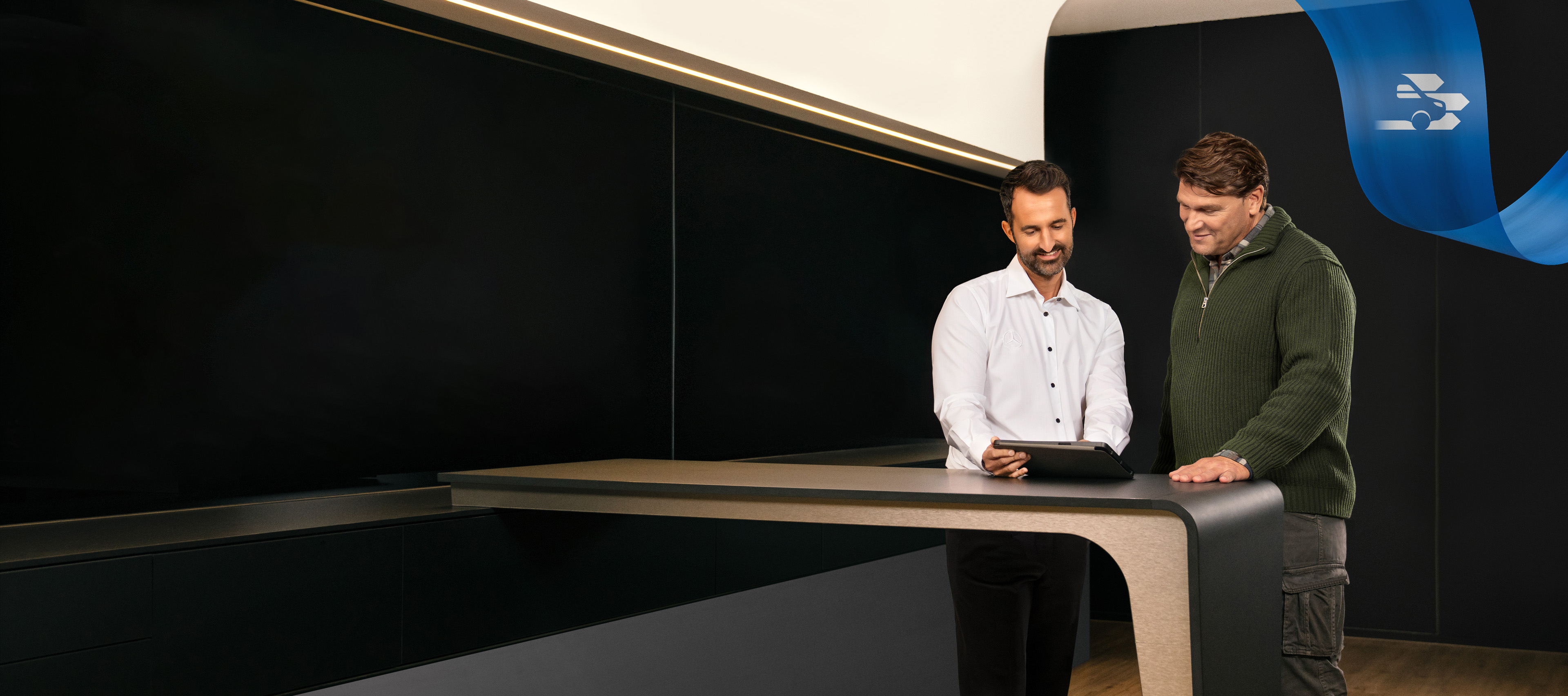 Mercedes-Benz | Pohodlí | Servisní partner Dva muži stojící v kanceláři servisního partnera Mercedes-Benz a diskutující o něčem, co vidí na tabletu