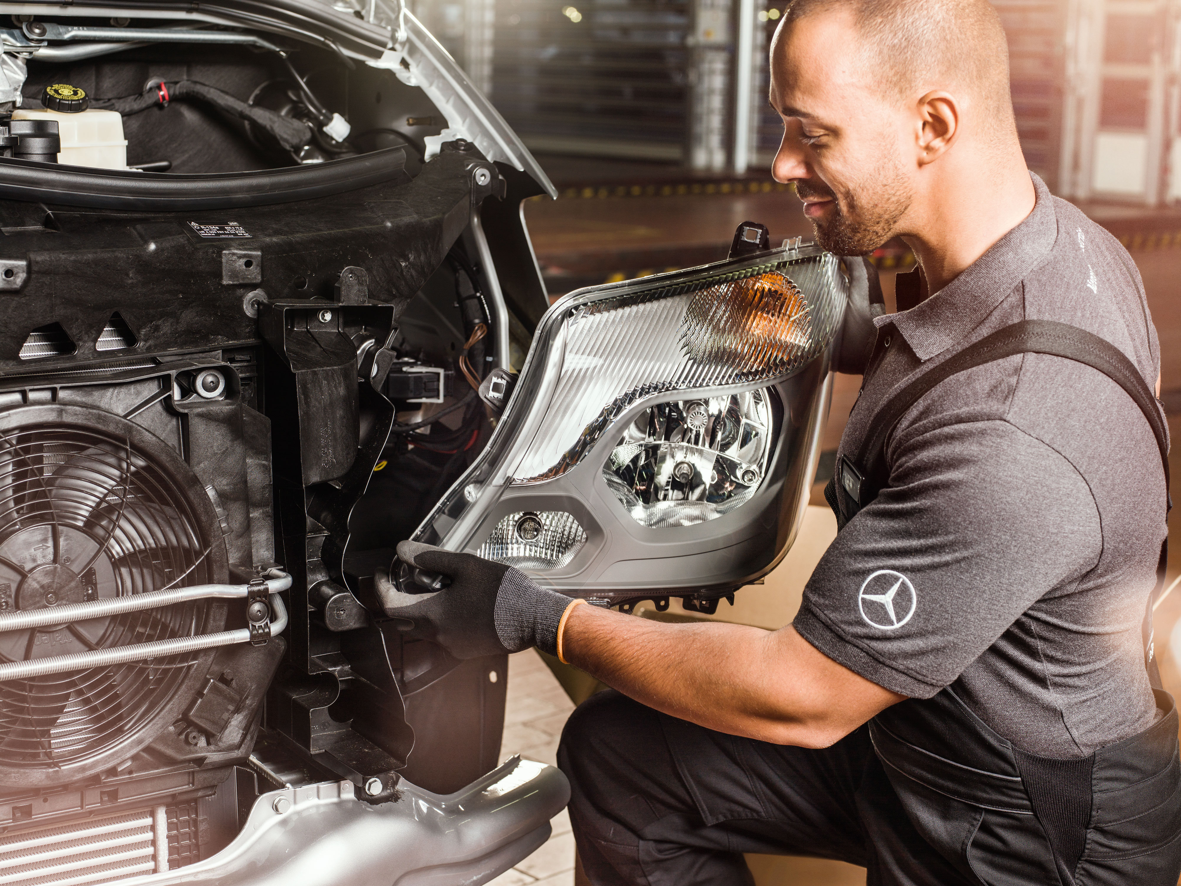Mercedes-Benz | Kvalita originálních dílů pro dodávková vozidla Mechanik kontroluje originální díly Mercedes-Benz před otevřeným motorem vozidla Sprinter a porovnává je s katalogem náhradních dílů Mercedes.