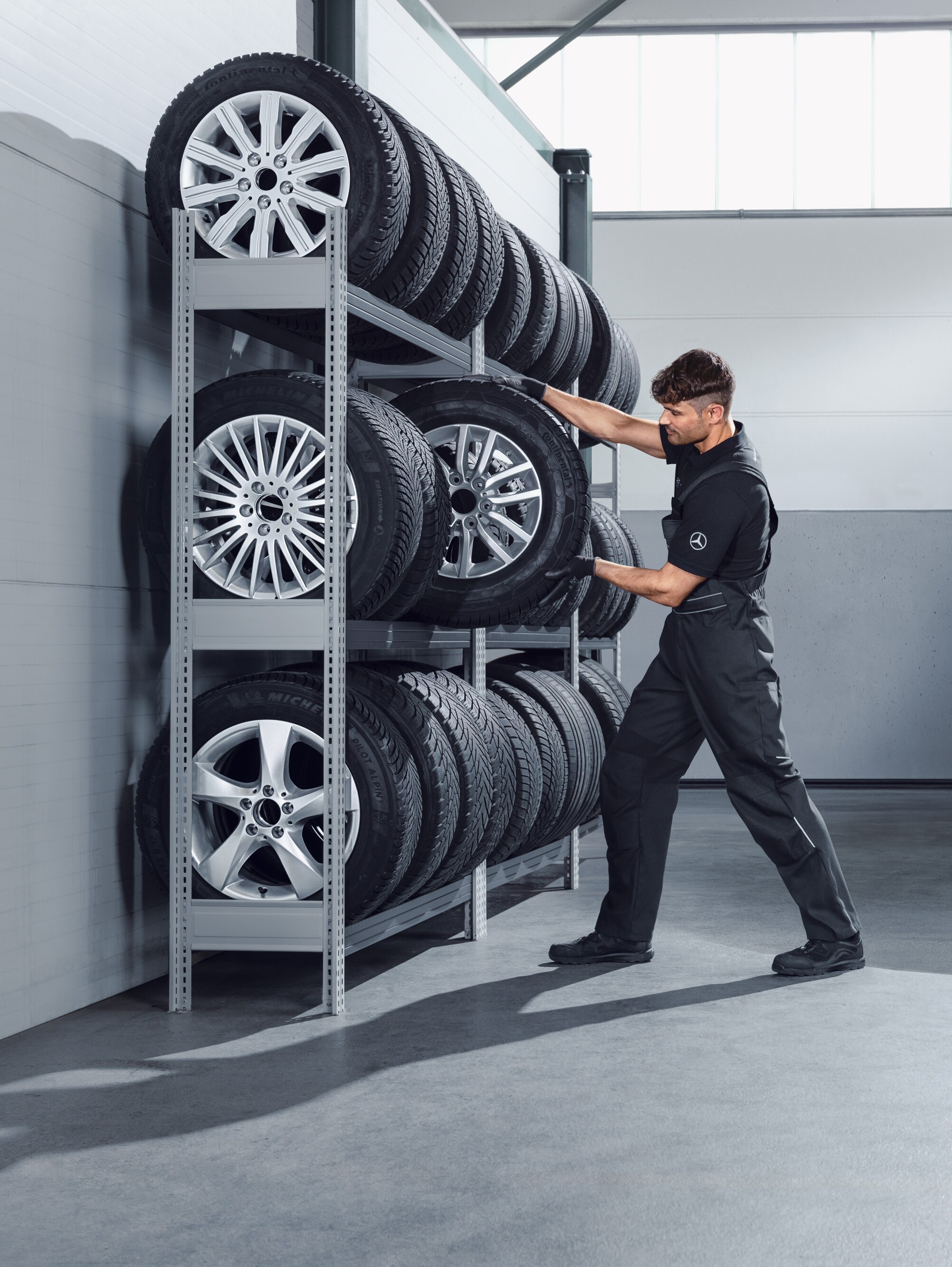 Mechanik vybírá z&nbsp;police v&nbsp;dílně kompletní zimní kola Mercedes-Benz pro bílý Sprinter.