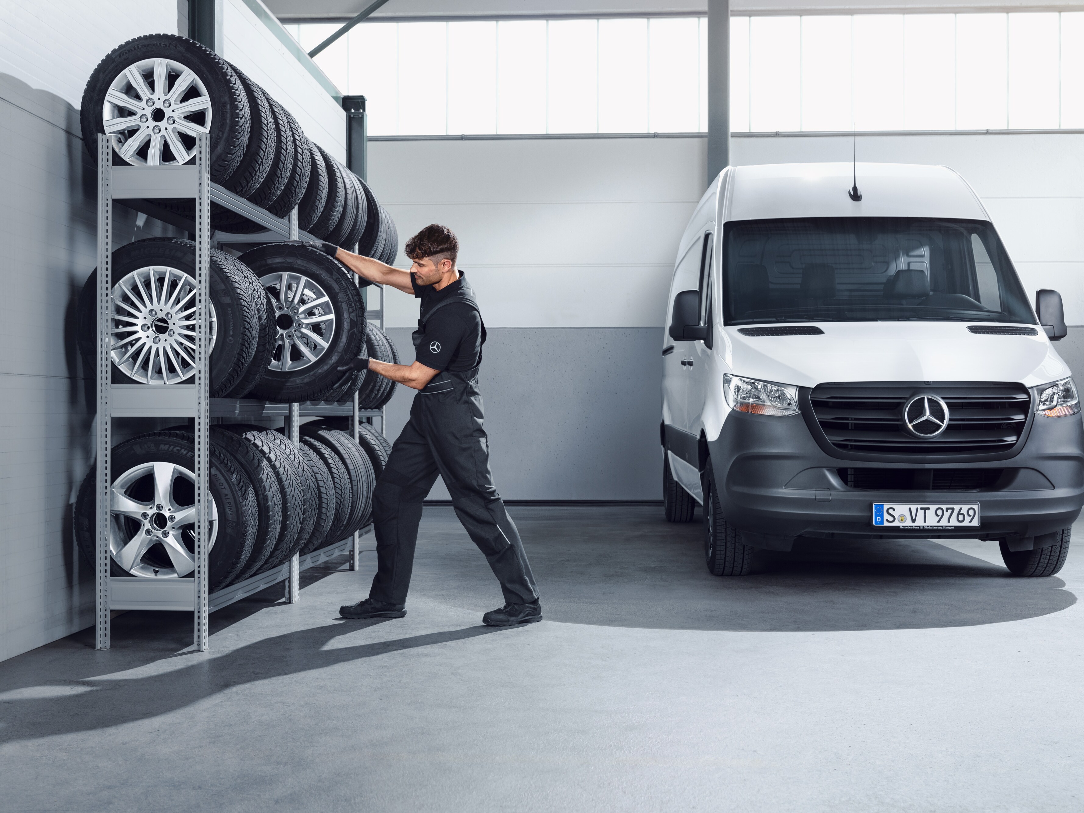 Mechanik vybírá z&nbsp;police v&nbsp;dílně kompletní zimní kola Mercedes-Benz pro bílý Sprinter.